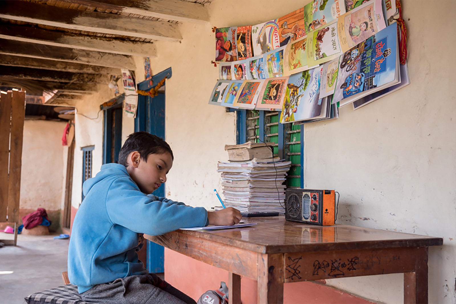 Young Pratik in blue hoodie writes with determination at wooden desk