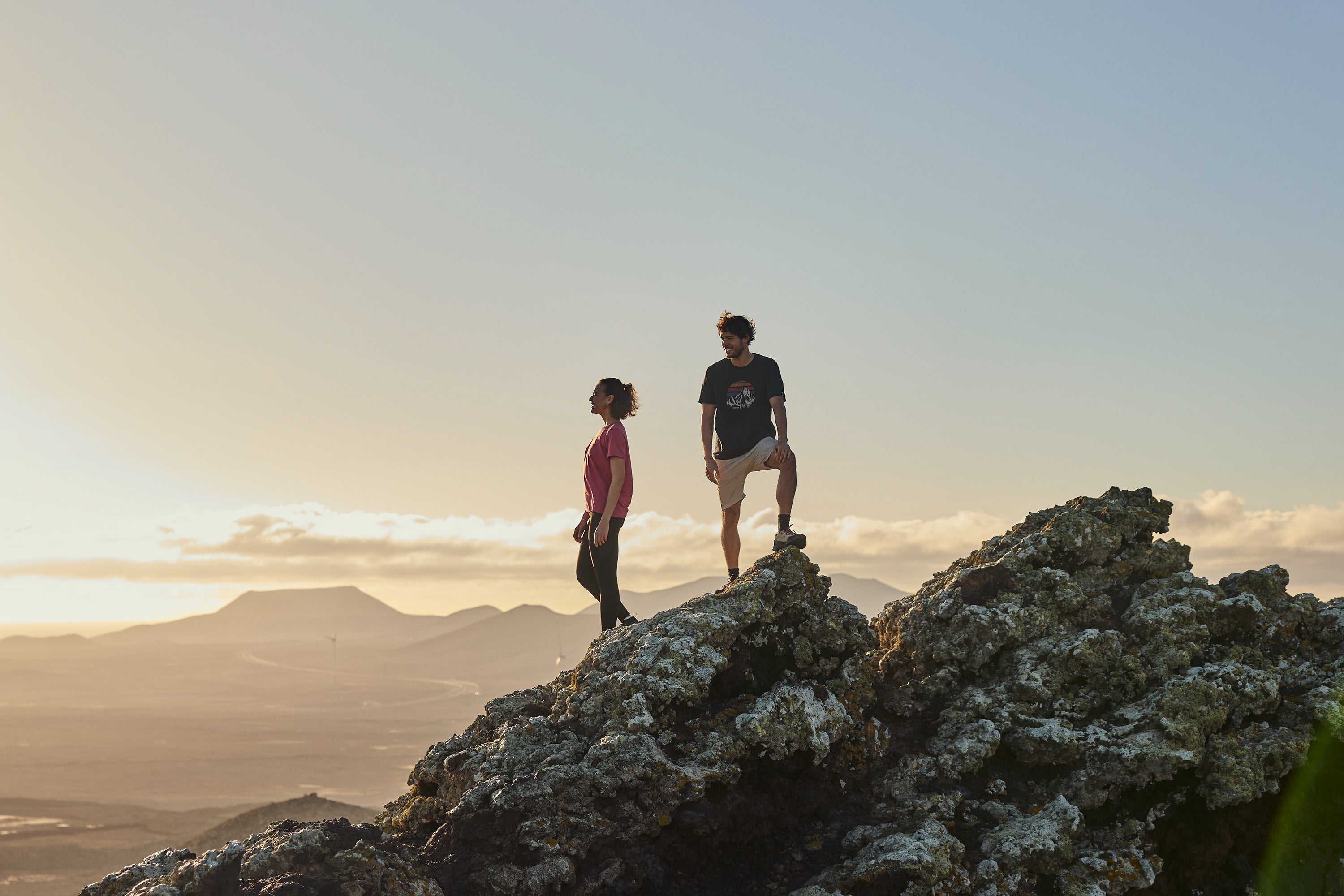 Two hikers atop volcanic rock at sunset in technical t-shirts