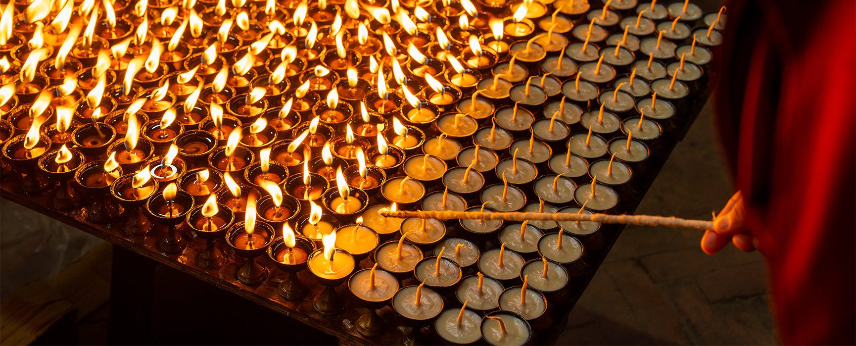 Hand tending flames of Gyalpo Losar oil lamps