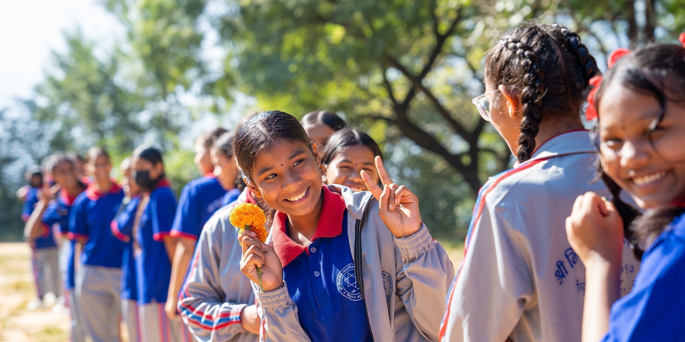 Smiling girl in blue gray school uniform holds orange marigold for International Women’s Day