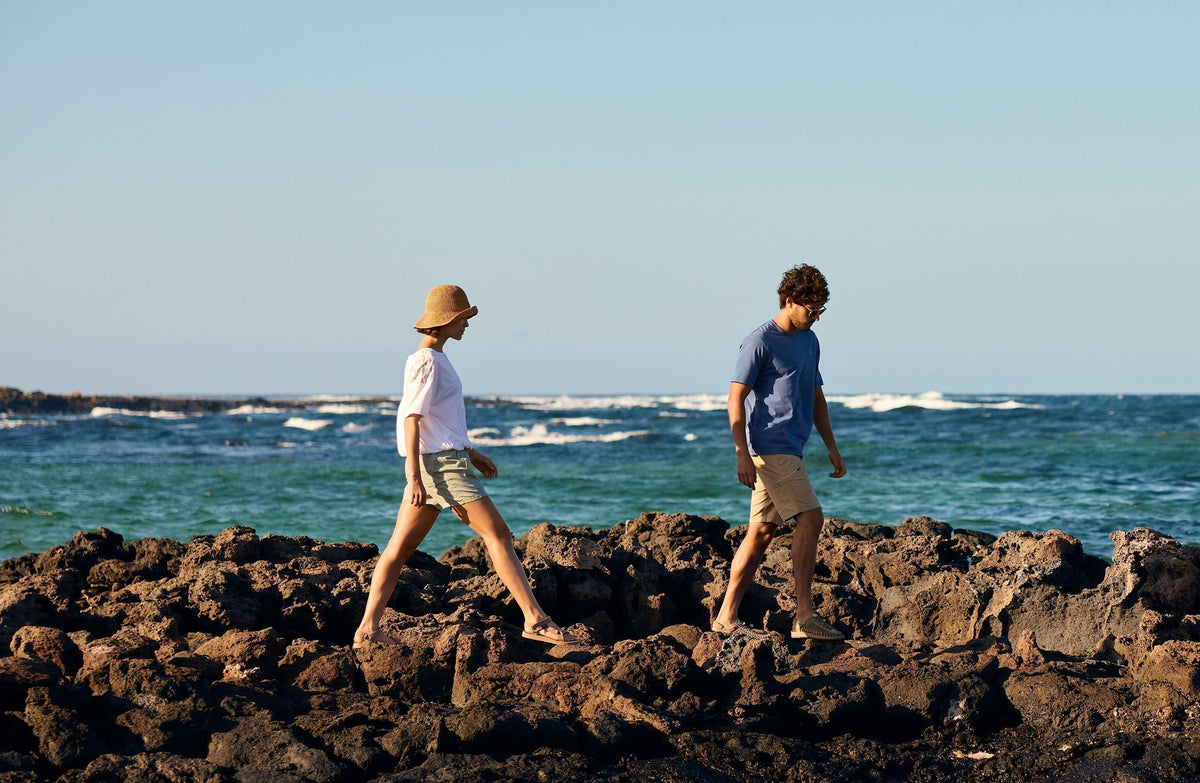 Man and woman walking barefoot on volcanic rocks by ocean for World Environment Day