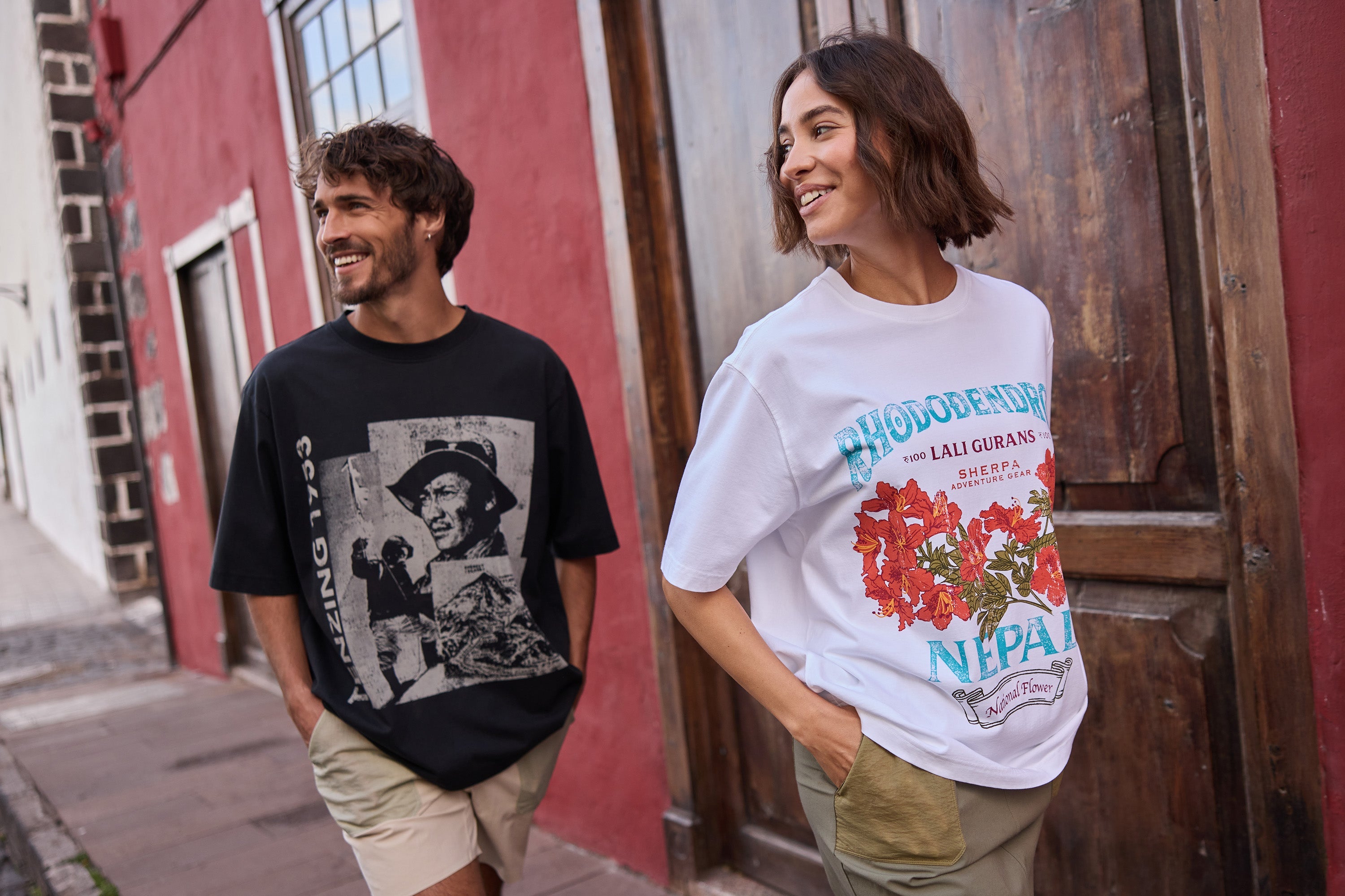 A man and woman walking down a road in Spain. The man is a black T-Shirt with a graphic of Tenzing Norgay printed on the front and the woman is wearing a white T-shirt with a rhododendron graphic.
