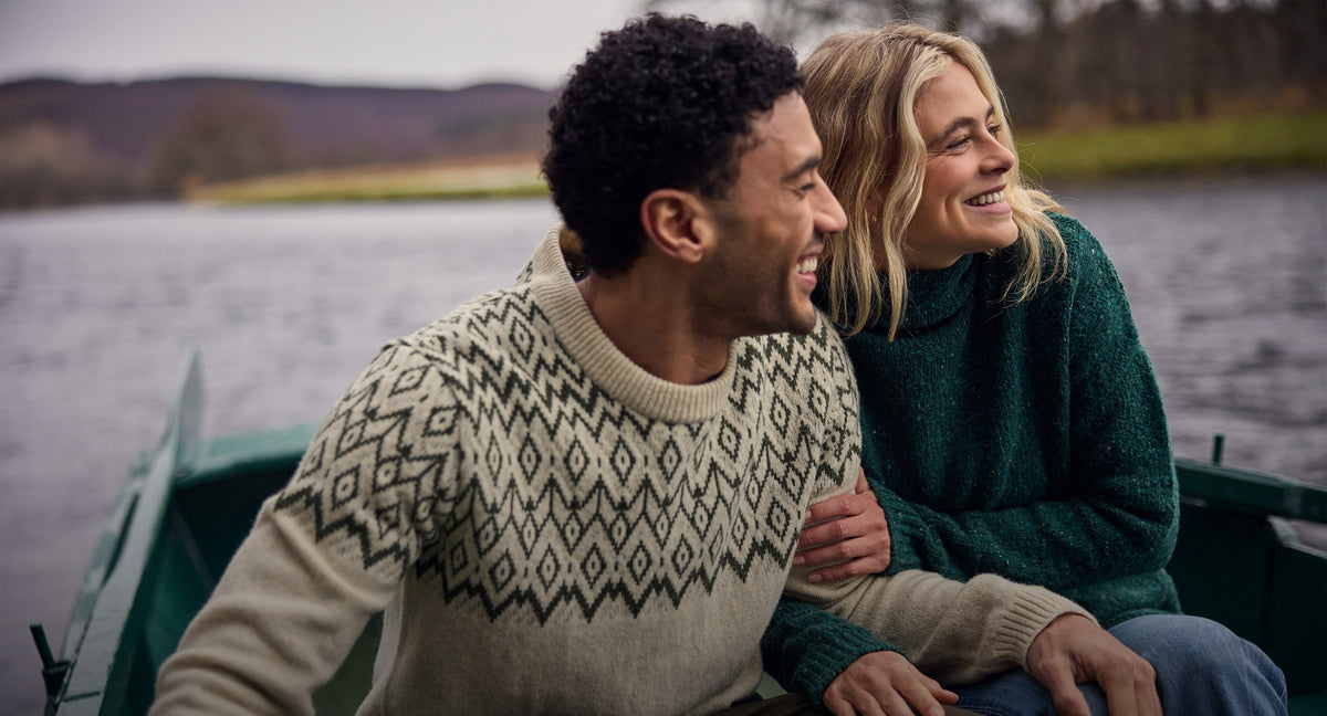 Couple outdoors wearing patterned cream and dark green knit sweaters.