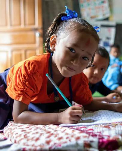 Close-up of a smiling school child in Nepal, writing in her school book.