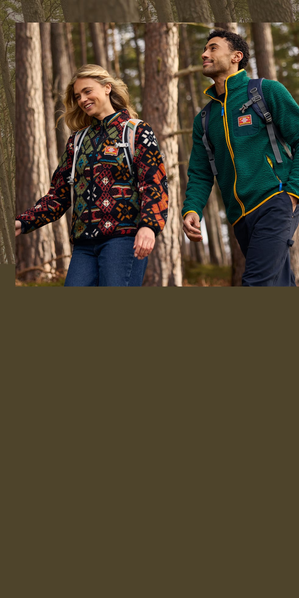 Man and woman walking through a pine forest, wearing patterned and green zip-up fleece jackets.