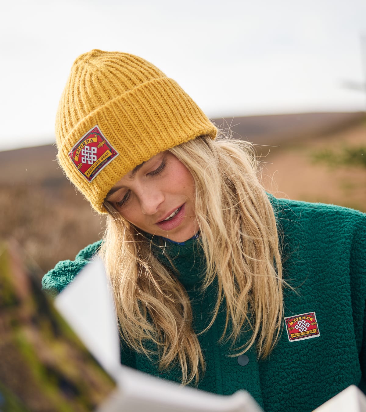 Woman in mustard knit beanie and green fleece jacket outdoors