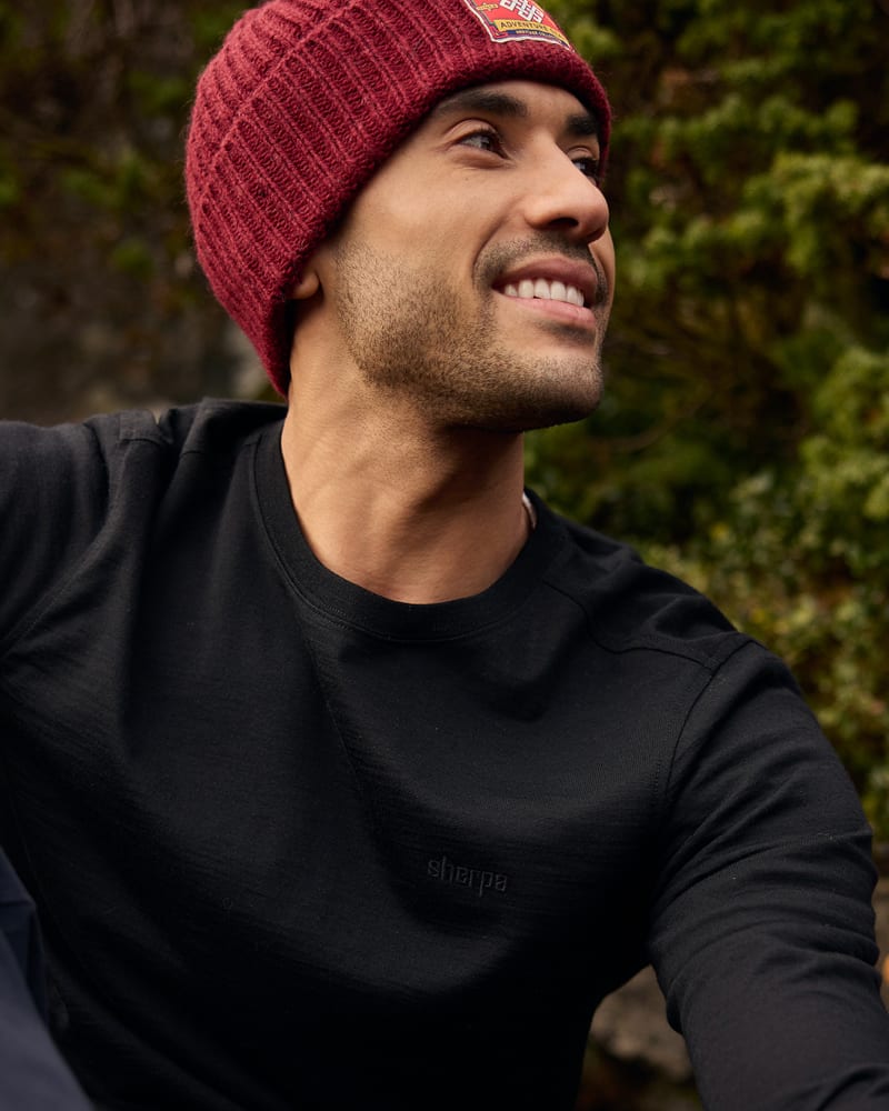 Smiling man in maroon ribbed beanie and black merino top outdoors