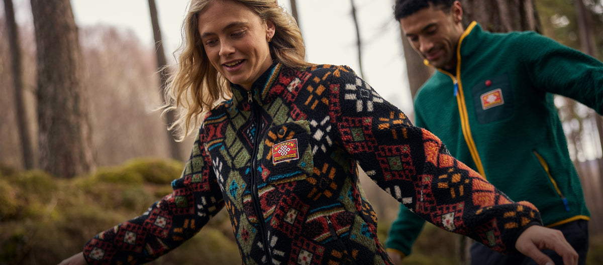 A woman in a colorful geometric patterned fleece jacket in a forest, with a man in a green fleece.