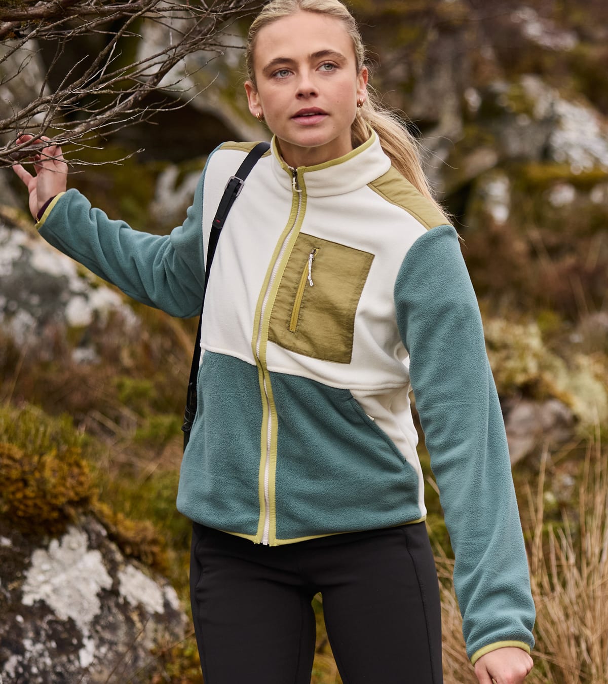 A woman wearing a color-block fleece jacket in teal, cream, and olive green.