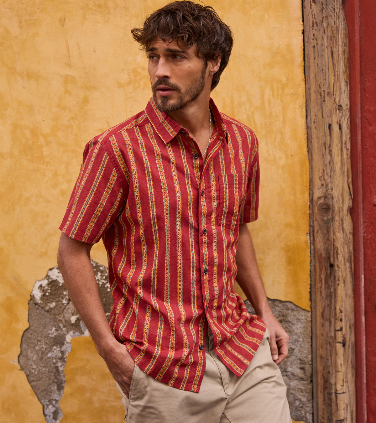 Man wearing a red and yellow striped shirt against a textured wall.