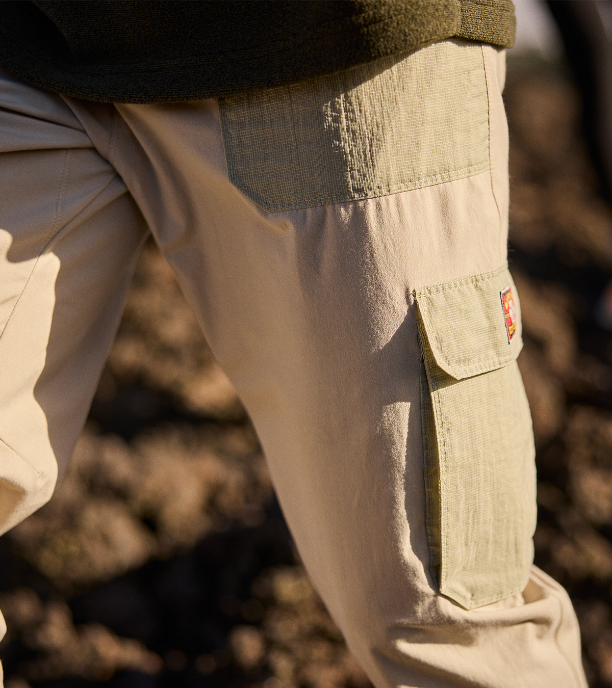 Person wearing beige cargo trousers with an olive waistband and leg pocket outdoors.