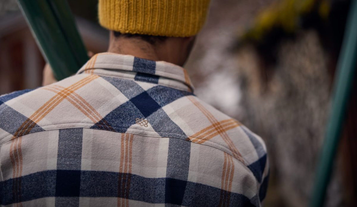 Person in a yellow knit beanie and navy, cream and orange plaid shirt, seen from behind.