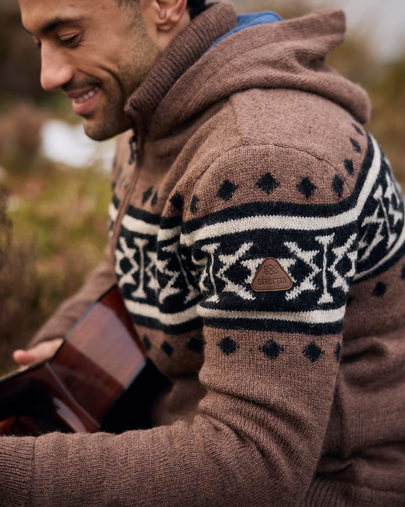 Man wearing a brown hooded knit sweater with a black and cream Fair Isle pattern, holding a guitar.