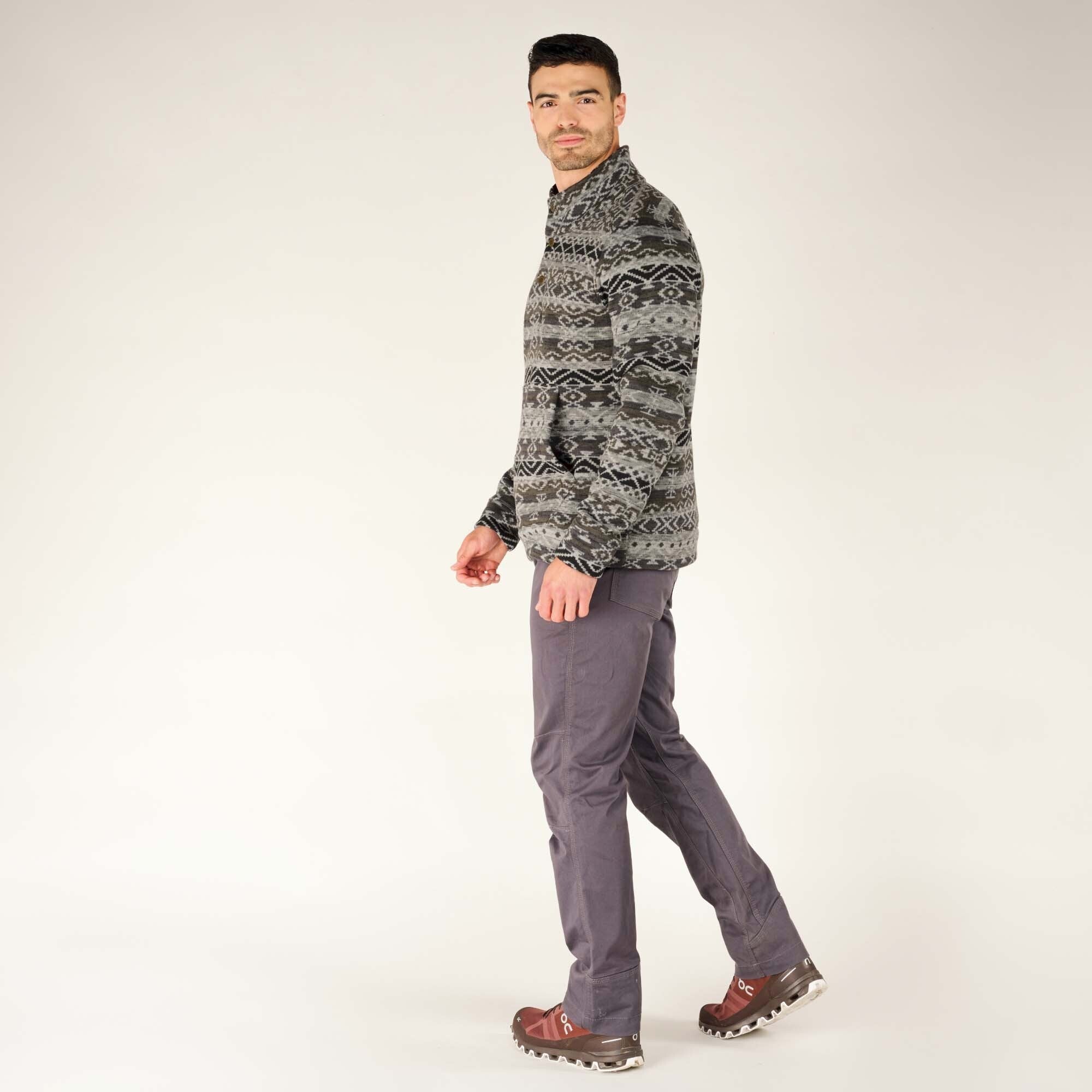 The model is mid-stride, showcasing the mobility and comfort of the Sherpa Adventure Gear Bhutan Pullover in Grey. The pairing with trousers and hiking shoes emphasises its practical yet stylish design for outdoor activities.