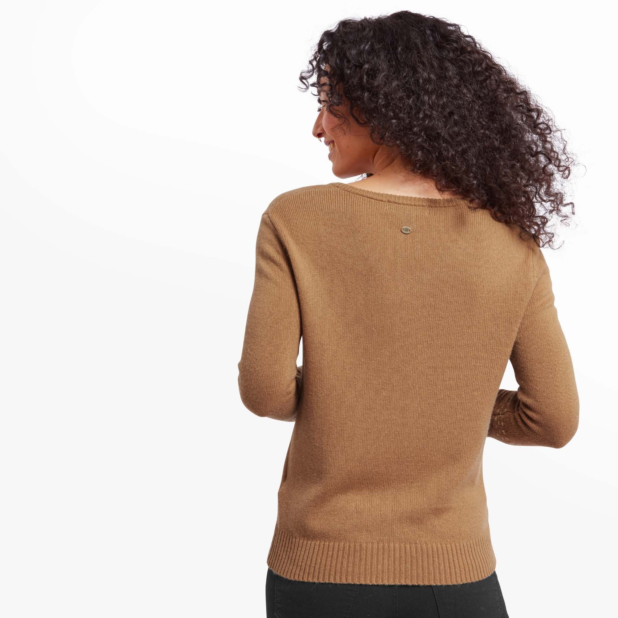 In the third image, the woman is captured from the back, showing the rear view of the Sherpa Adventure Gear Maya V-Neck Sweater in Light Brown. It highlights the plain design on the back, with a small circular logo detail near the neckline. Her curly hair falls over her shoulders, complementing the simple elegance of the outfit.
