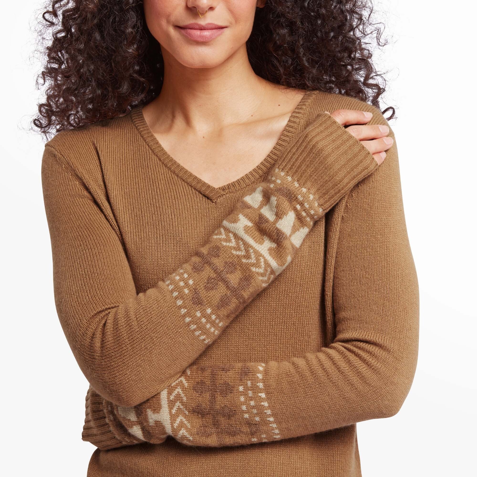 The fourth image provides a close-up view of the Sherpa Adventure Gear Maya V-Neck Sweater in Light Brown’s sleeve pattern. The intricate geometric designs in beige and white are prominently displayed on the light brown base. This detail emphasises the craftsmanship and unique character of the sweater. The woman is crossing her arms, making the sleeve patterns the focal point.