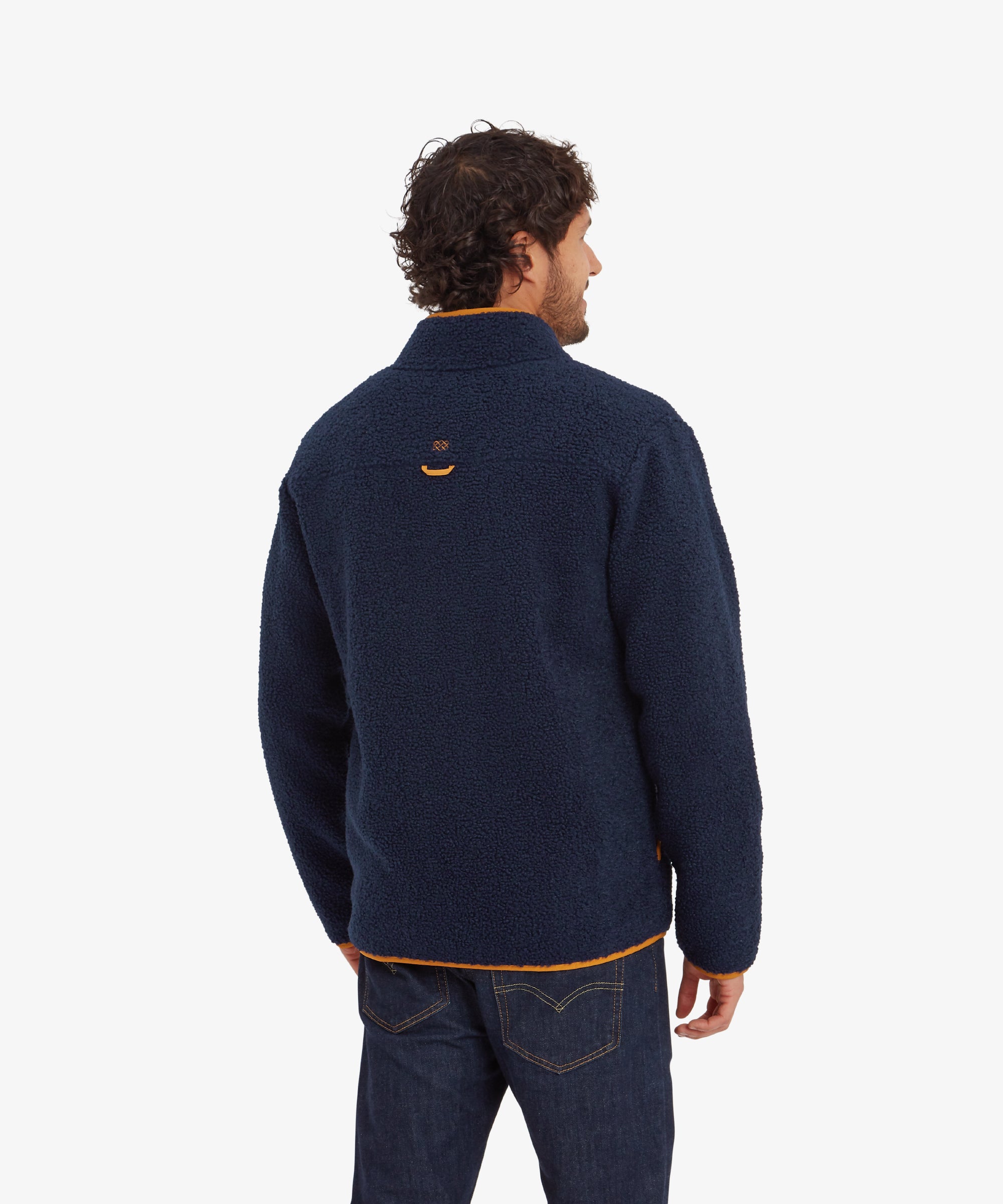 A back view of the Sherpa Adventure Gear Yatri Full Zip Jacket in Blue, showing the plain back with an embroidered Sherpa logo and a small orange loop. The orange piping along the hem contrasts against the dark fleece material.