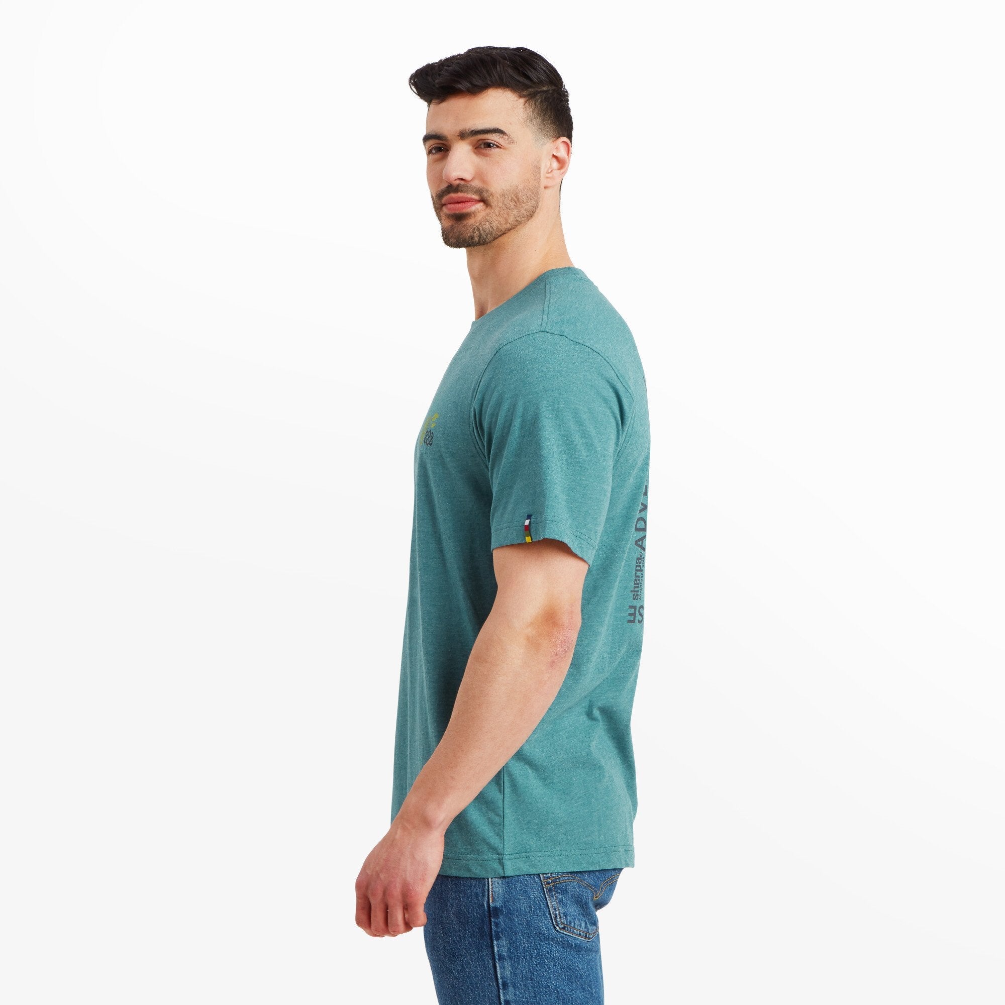 A profile shot of the man wearing the same Sherpa Adventure Gear Purpose T-Shirt in Blue. The side view showcases the clean fit of the shirt along the shoulders and torso, as well as the small Sherpa Adventure Gear logo flag detail on the sleeve.
