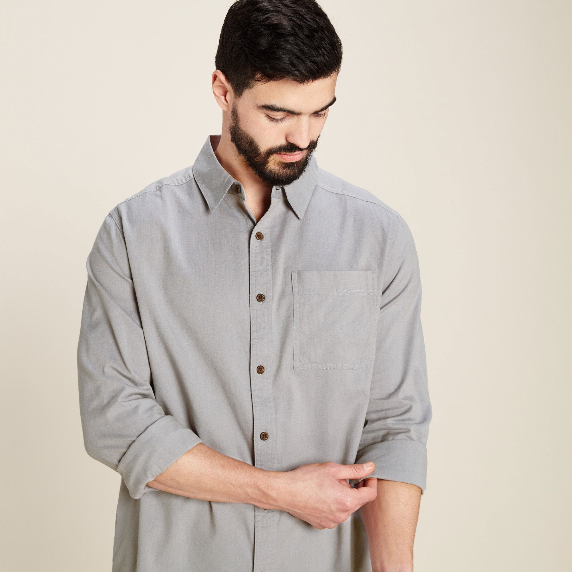 A close-up and casual look of the man rolling up his sleeves, demonstrating the Sherpa Adventure Gear Tharu Long Sleeve Shirt in Grey's versatility and comfortable fit. The fabric's texture and button details are clearly visible, emphasising its high-quality finish.