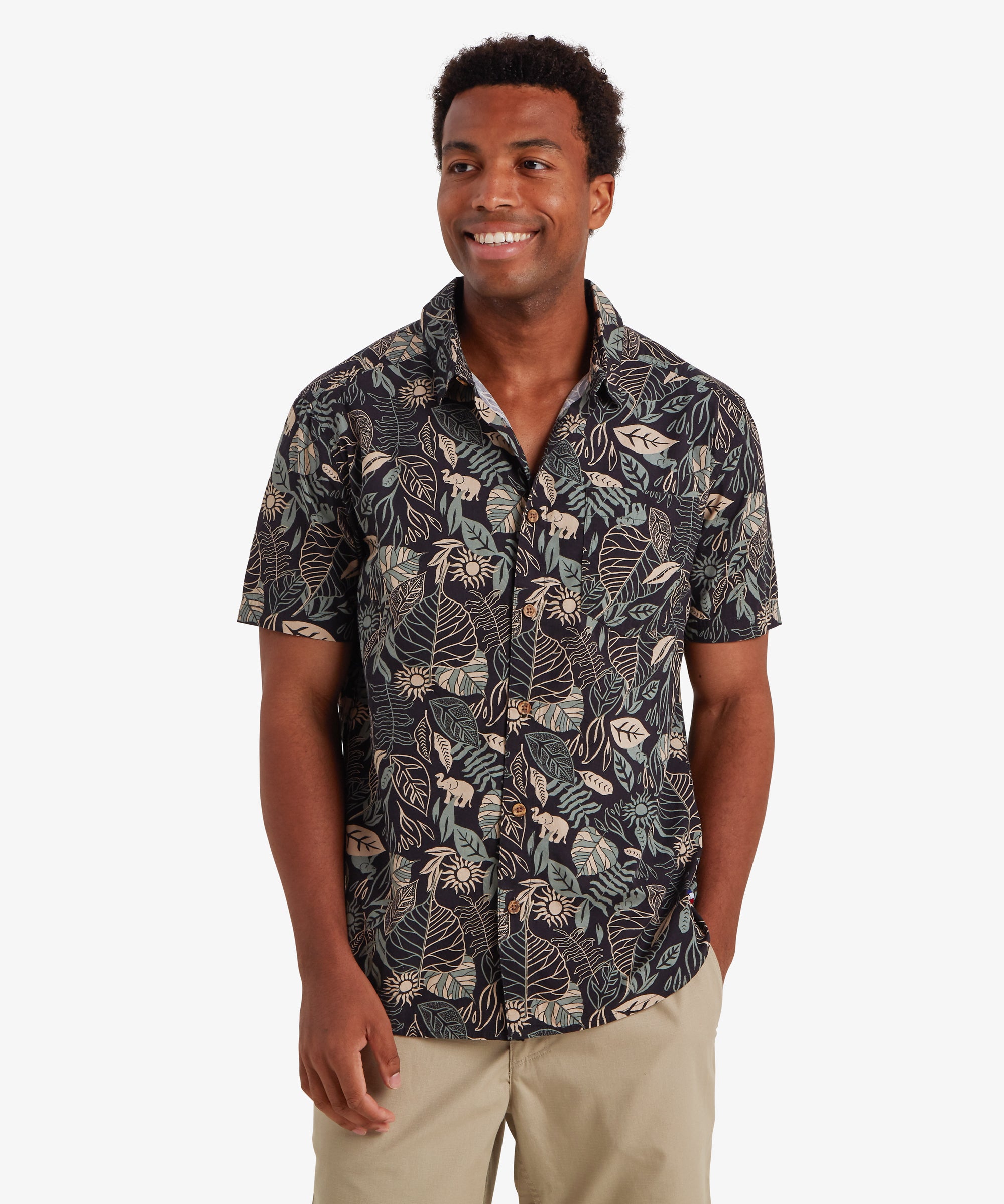 Mann mit schwarzem Kurzarmhemd mit Knšpfen und Blattmuster in zarten Wei§-, GrŸn- und Blautšnen. Die oberen beiden Knšpfe sind offen. Das klassisch geschnittene Hemd wird mit beigen Shorts zu einem sommerlichen Alltagslook kombiniert. Der Mann steht lŠchelnd da, blickt leicht nach links, eine Hand entspannt an der Seite, die andere in der Hosentasche. Er steht vor einem wei§en Hintergrund.