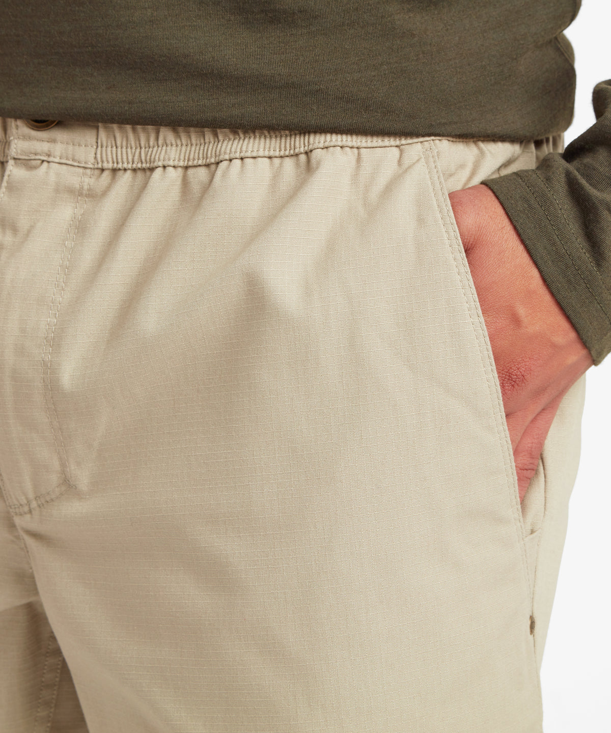 Nahaufnahme der Vordertasche und des elastischen Bunds der beigen Hose, die den strukturierten Stoff und die genŠhte Taschenšffnung hervorheben.