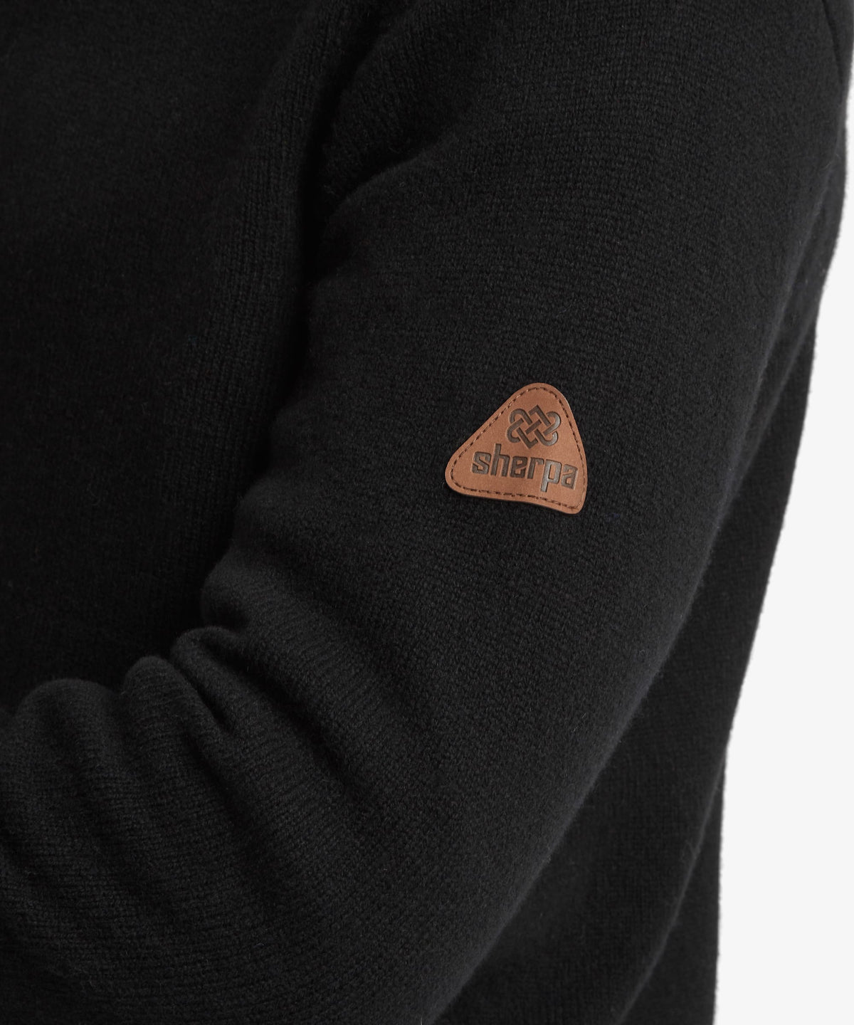 Close-up of a black knit sweater sleeve featuring a small brown triangular patch with the brand.