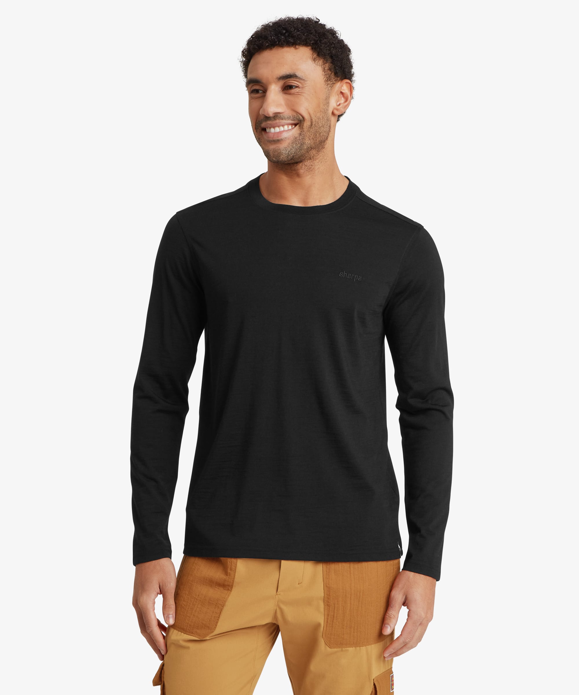 A man wearing a black long-sleeve crewneck t-shirt and tan cargo pants, standing against a light gray background.