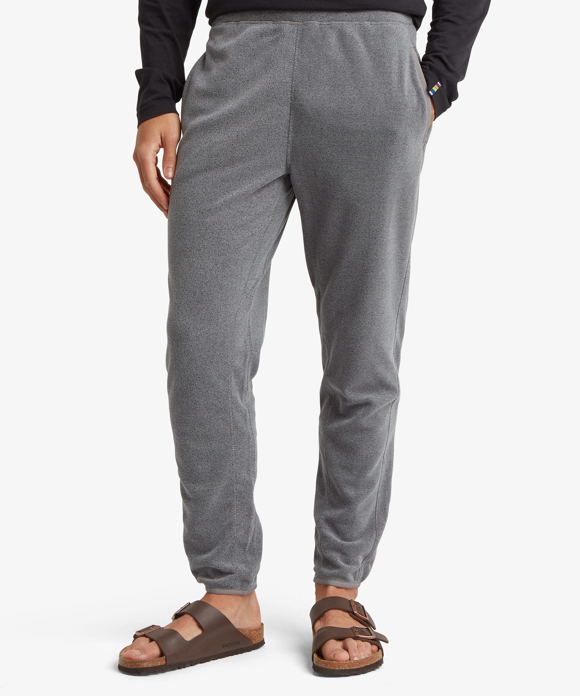Front view of grey fleece jogger pants featuring an elastic waistband, tapered legs, ribbed cuffs, and side hand pockets. Styled with sandals and a dark long-sleeve top.