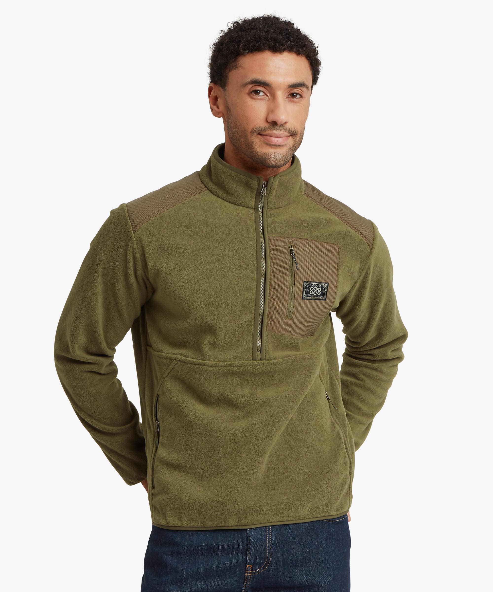 A man wearing an olive green quarter-zip fleece pullover with brown shoulder panels and a small logo patch on the chest pocket, paired with blue jeans against a light gray background.