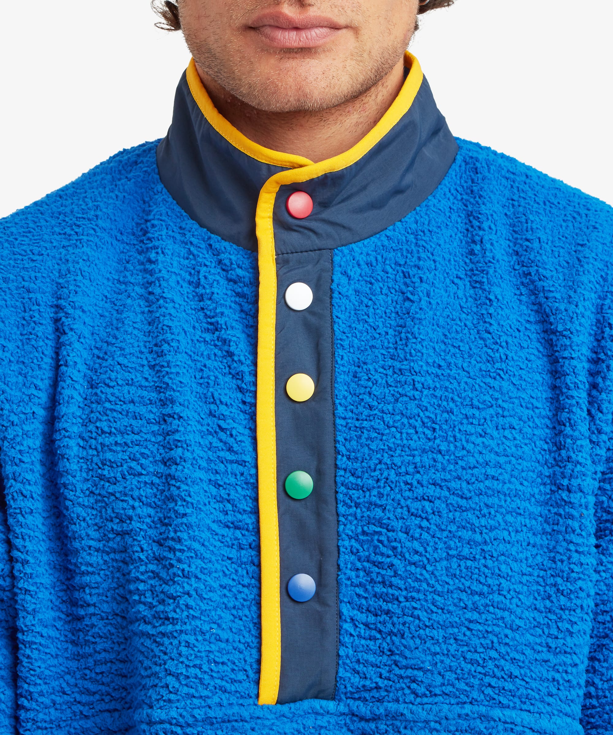 Close-up of a male model wearing the Sherpa Tarcho Snap Pullover in blue, highlighting the textured fleece fabric, stand collar, contrast facing and colourful snap-button placket.