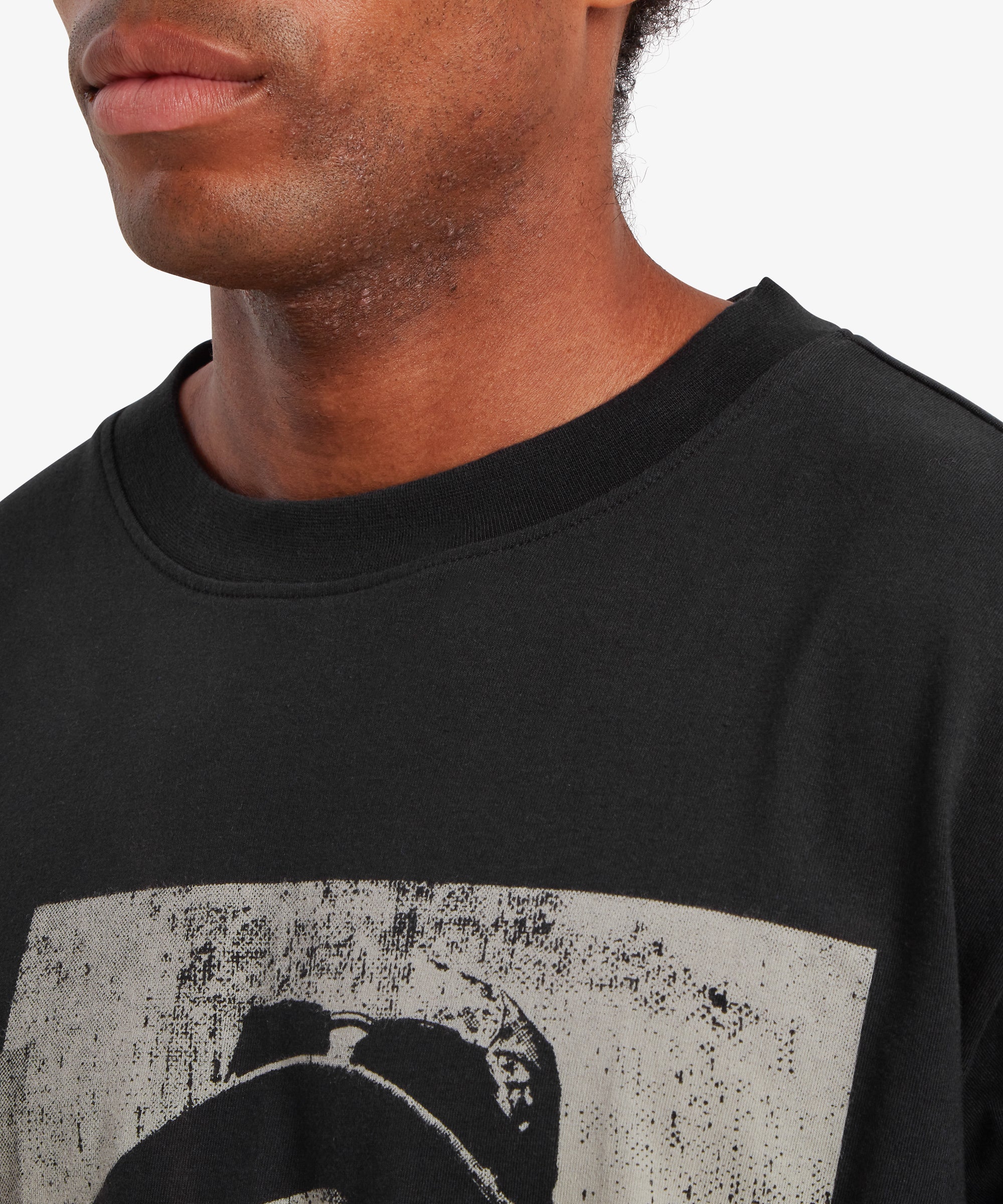 A close up of a man wearing a relaxed fit, black T-shirt. The collar and the top of the T-shirt are visible. A graphic can be seen on the front of the T-shirt depicting Tenzing Sherpa and the number "1953" written vertically down the left side.