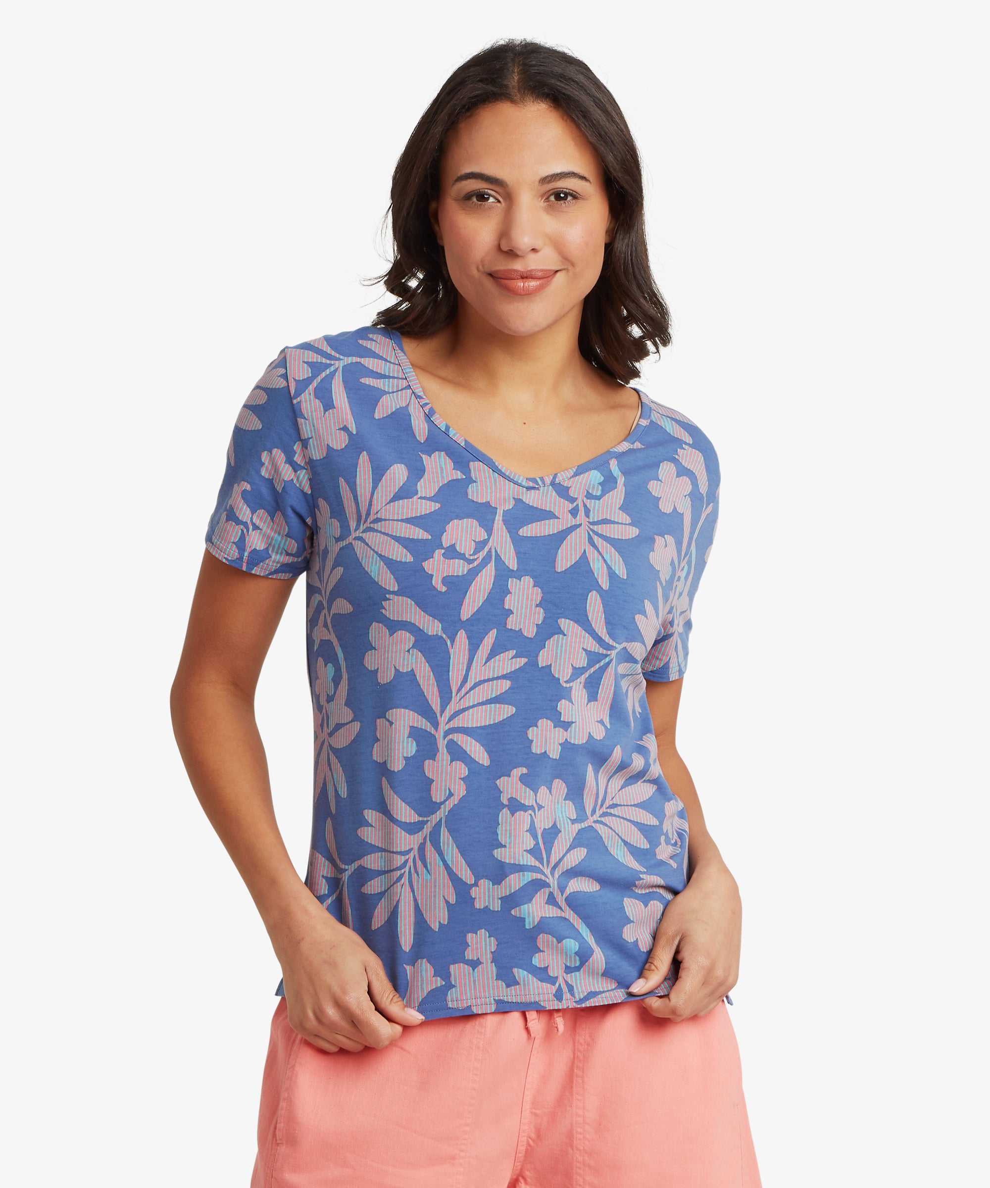 Woman standing facing forward wearing a blue floral V-neck T-shirt with short sleeves and a relaxed, easy fit through the torso.