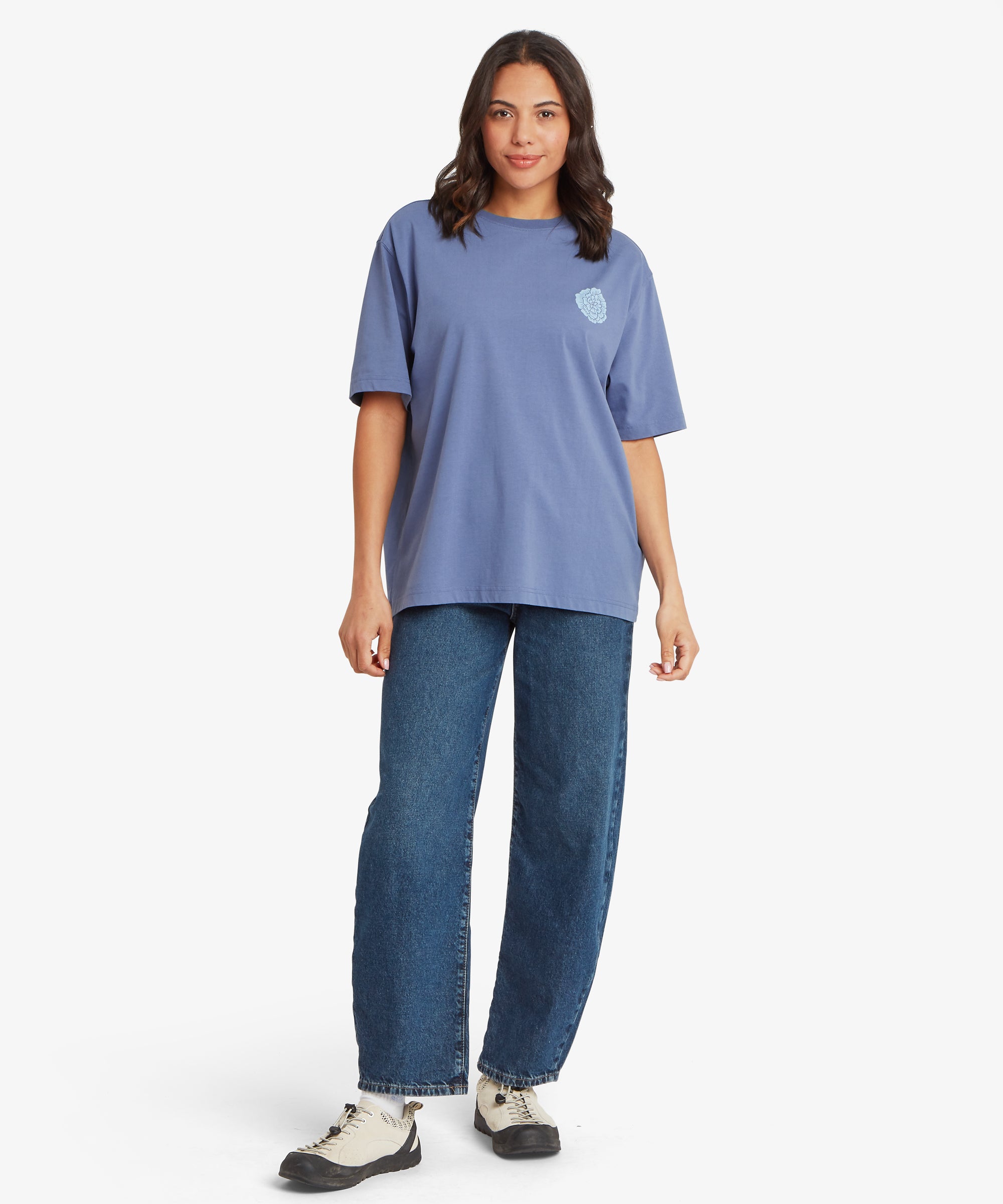 Full-body view of blue T‑shirt with small chest graphic, paired with relaxed-fit blue jeans and light sneakers.