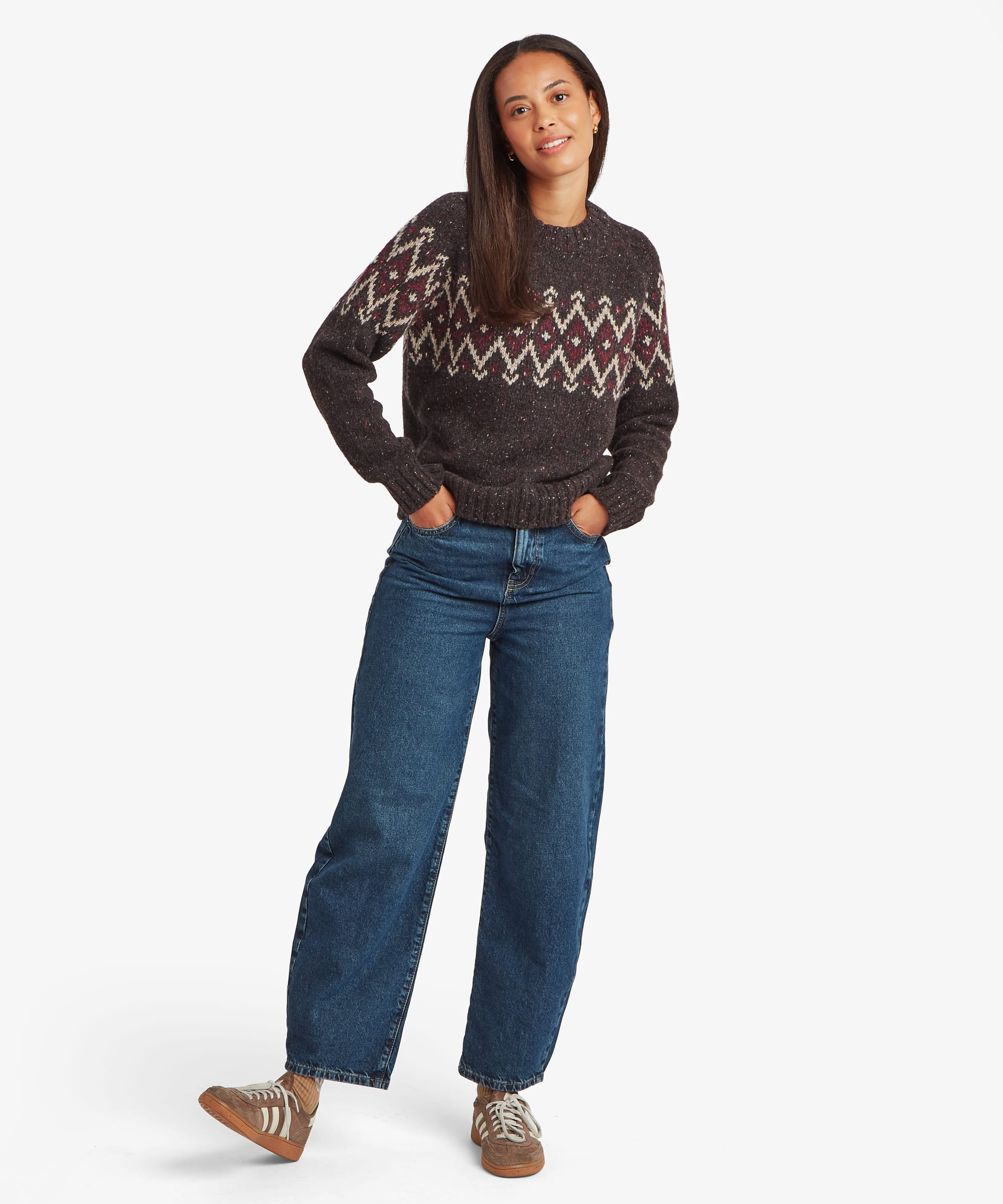 Full-body front view of a woman wearing a dark Fair Isle sweater paired with blue jeans. The sweater features a traditional Nordic-inspired yoke design and a relaxed everyday fit.