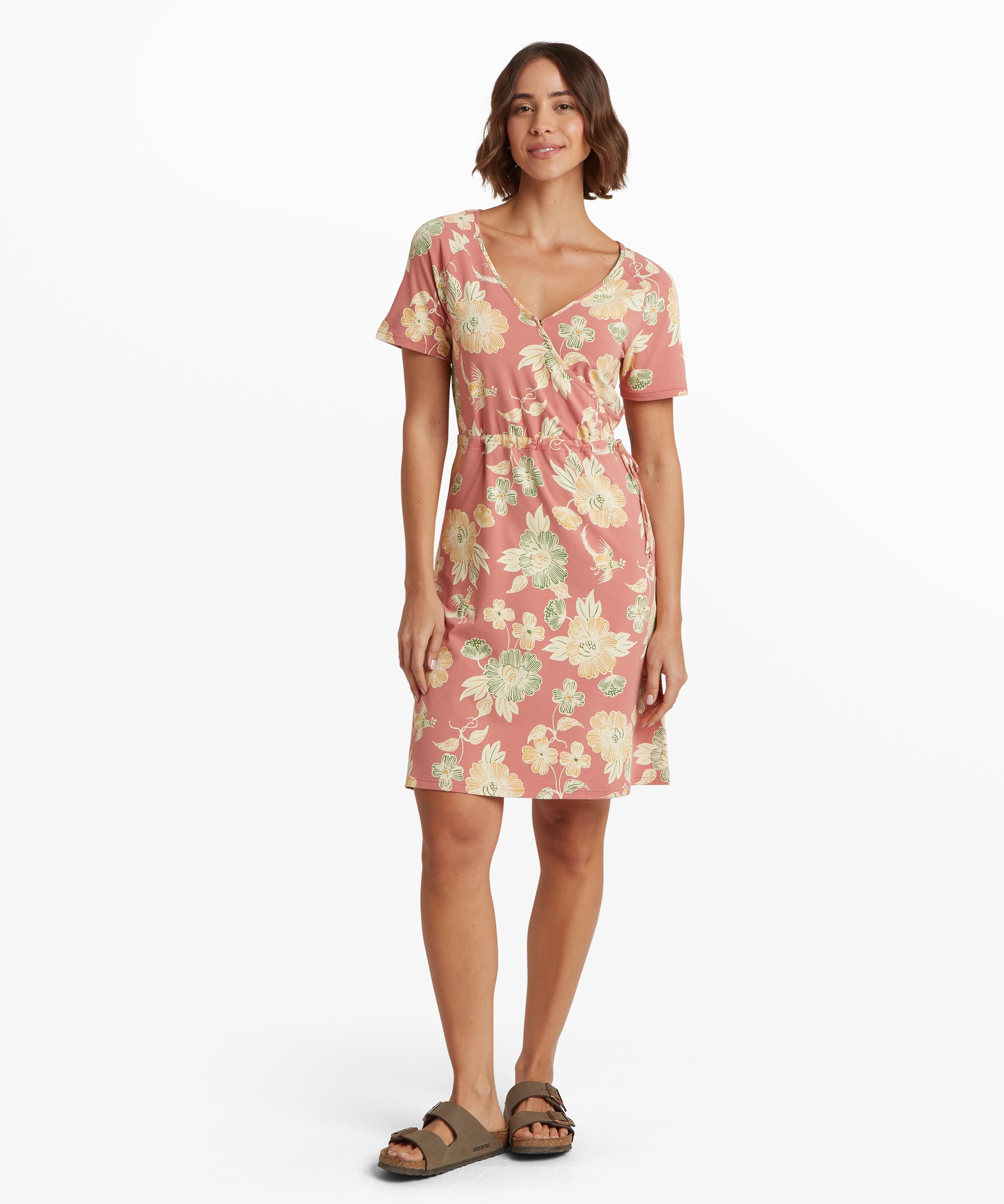 Side view of a mid‑length dress in soft pink featuring a tonal scenic illustration print and two side pockets. The dress has a gentle A‑line shape and is styled with sandals.