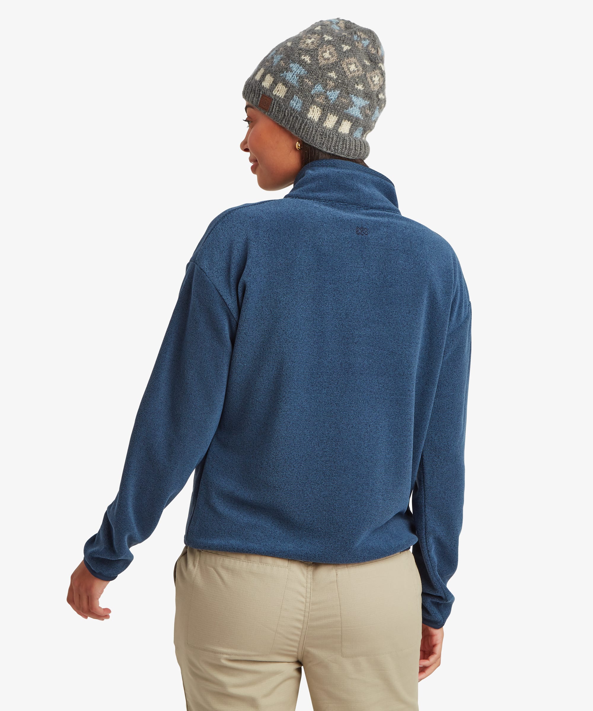 Rear view of a woman wearing the Sherpa Rolpa 1/2-Zip Pullover in blue with a patterned beanie. The image highlights the clean back design and comfortable fleece construction.