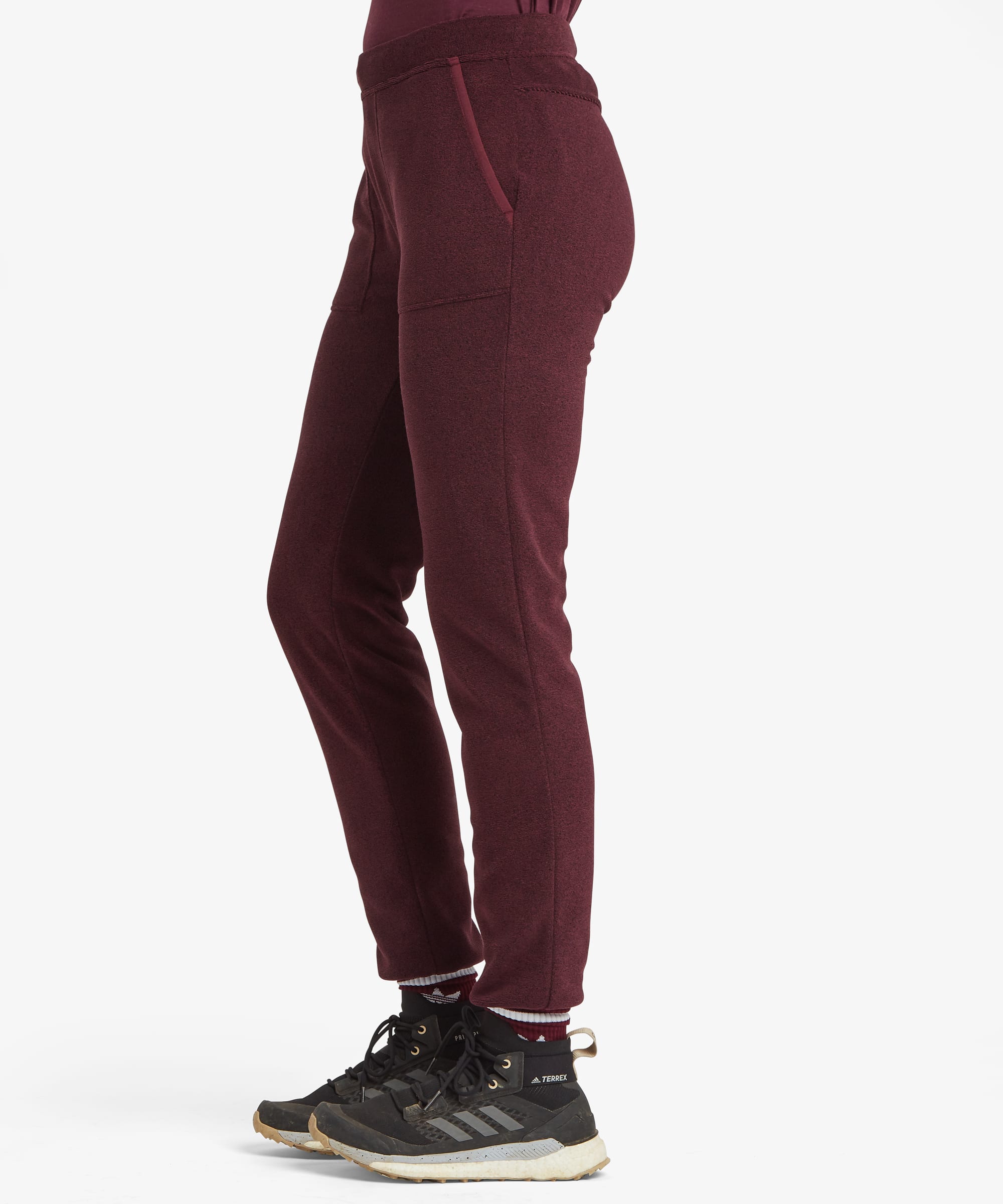 Side profile view of a woman wearing the Sherpa Rolpa Jogger in burgundy red. The image showcases the tapered silhouette, elasticated waistband and comfortable fit.