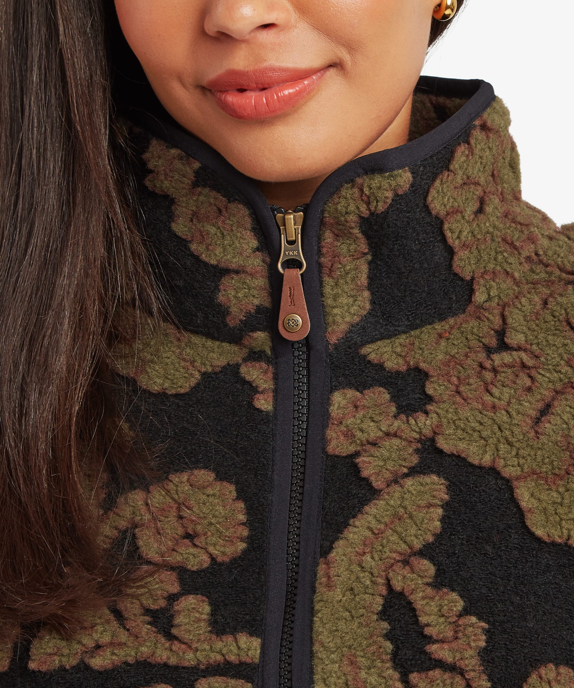 Close-up portrait of a woman wearing a dark green floral-patterned quarter-zip fleece pullover. The image focuses on the high collar, front zip closure, and textured floral design around the neckline and chest.