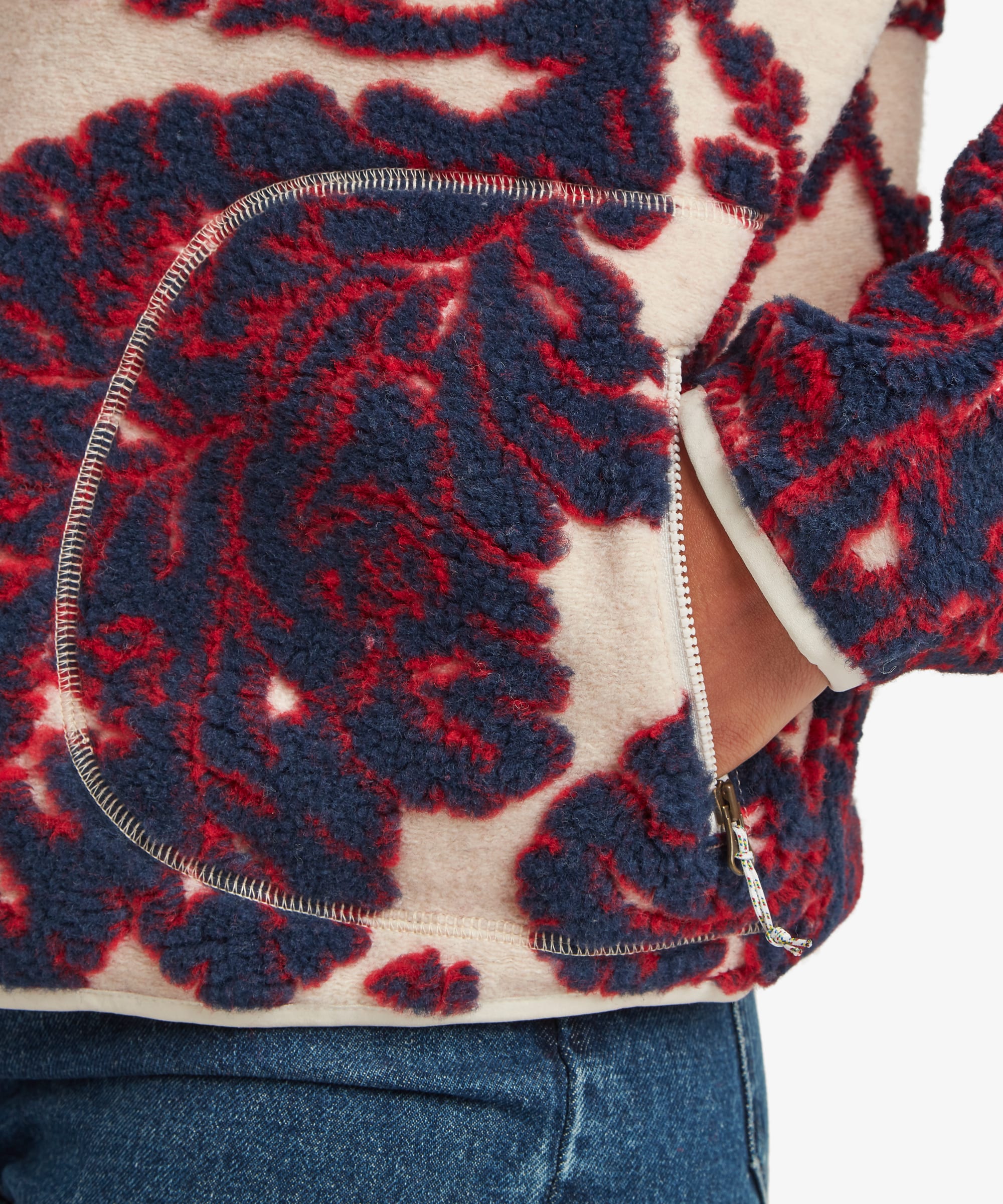 Detailed fabric close-up of the cream fleece jacket highlighting the bold burgundy floral pattern, soft fleece texture, and seam construction near the hem.