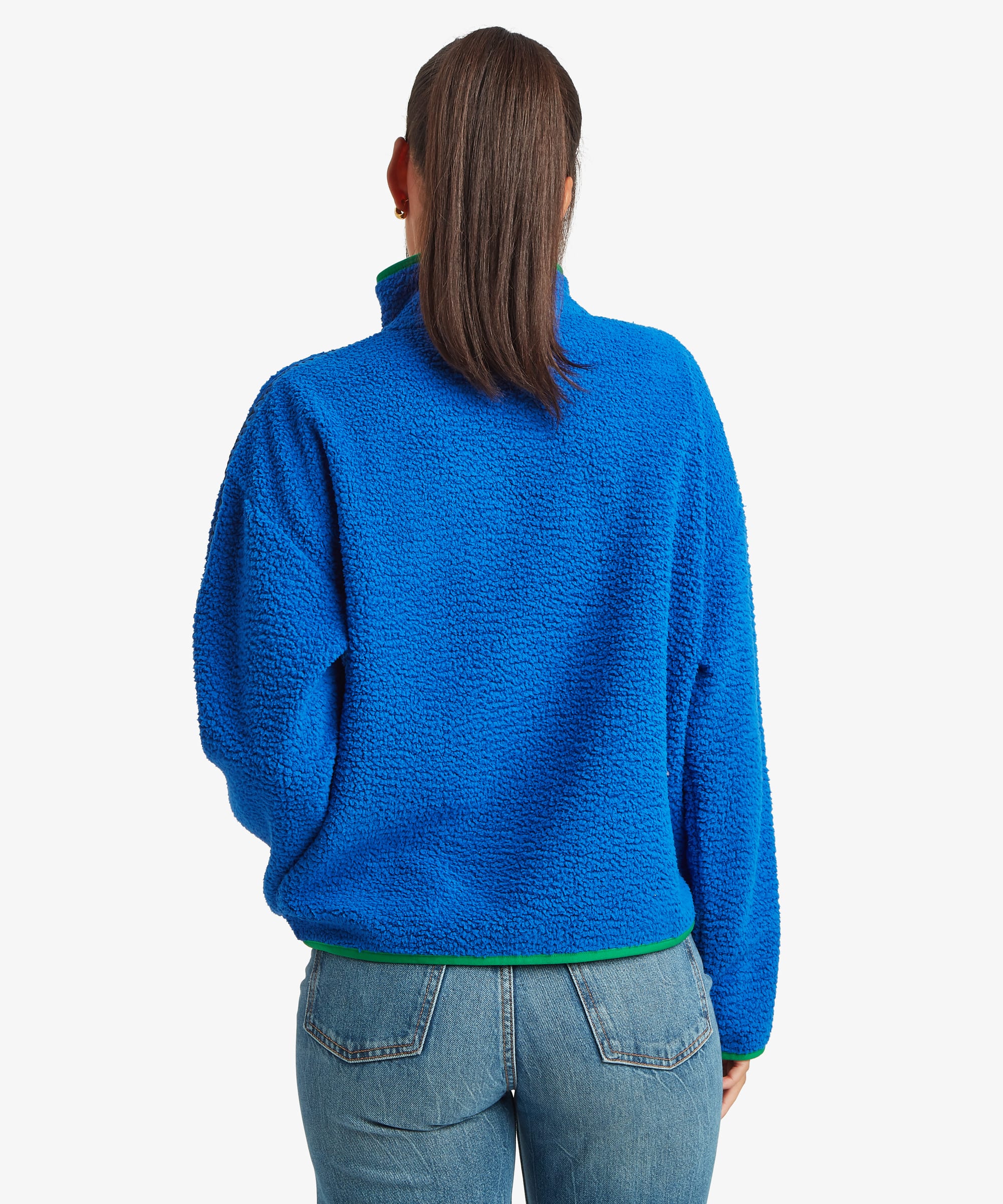 Rear studio view of a woman wearing a bright blue quarter-zip fleece pullover paired with blue jeans. The image highlights the clean back design, relaxed fit, and high collar.