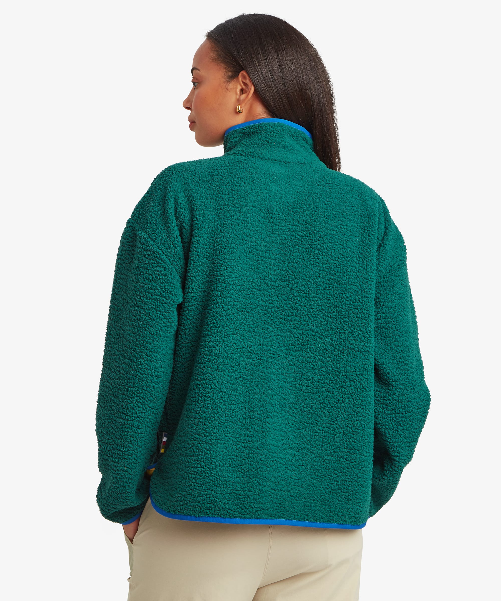 Back view of a woman wearing a deep green fleece jacket paired with beige trousers. The image displays the clean back panel, relaxed shape, and full coverage of the garment.