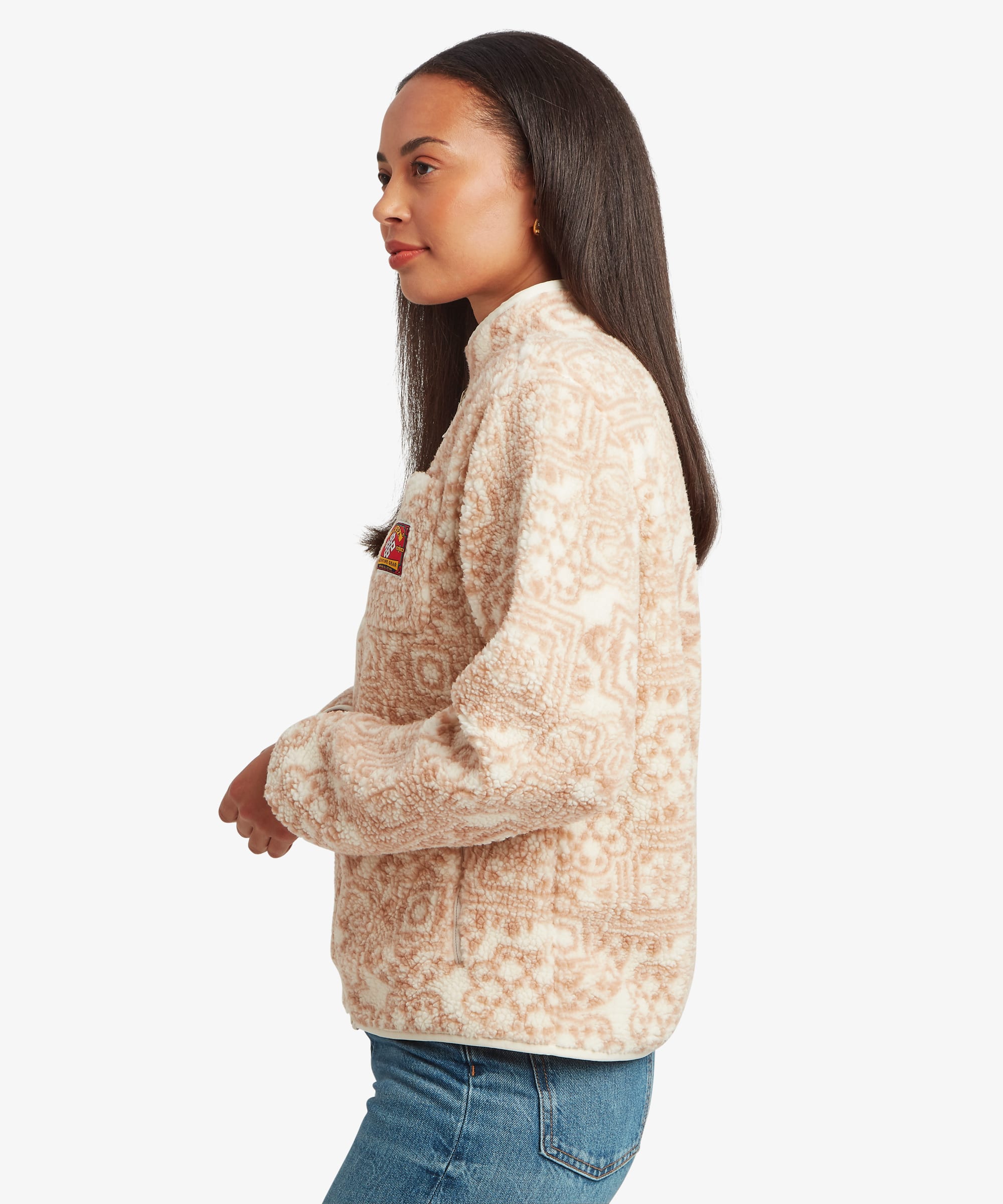 Side-profile studio image of a woman wearing a cream fleece jacket with an all-over tonal geometric pattern. The view highlights the jacket's shape, collar height, and relaxed silhouette.