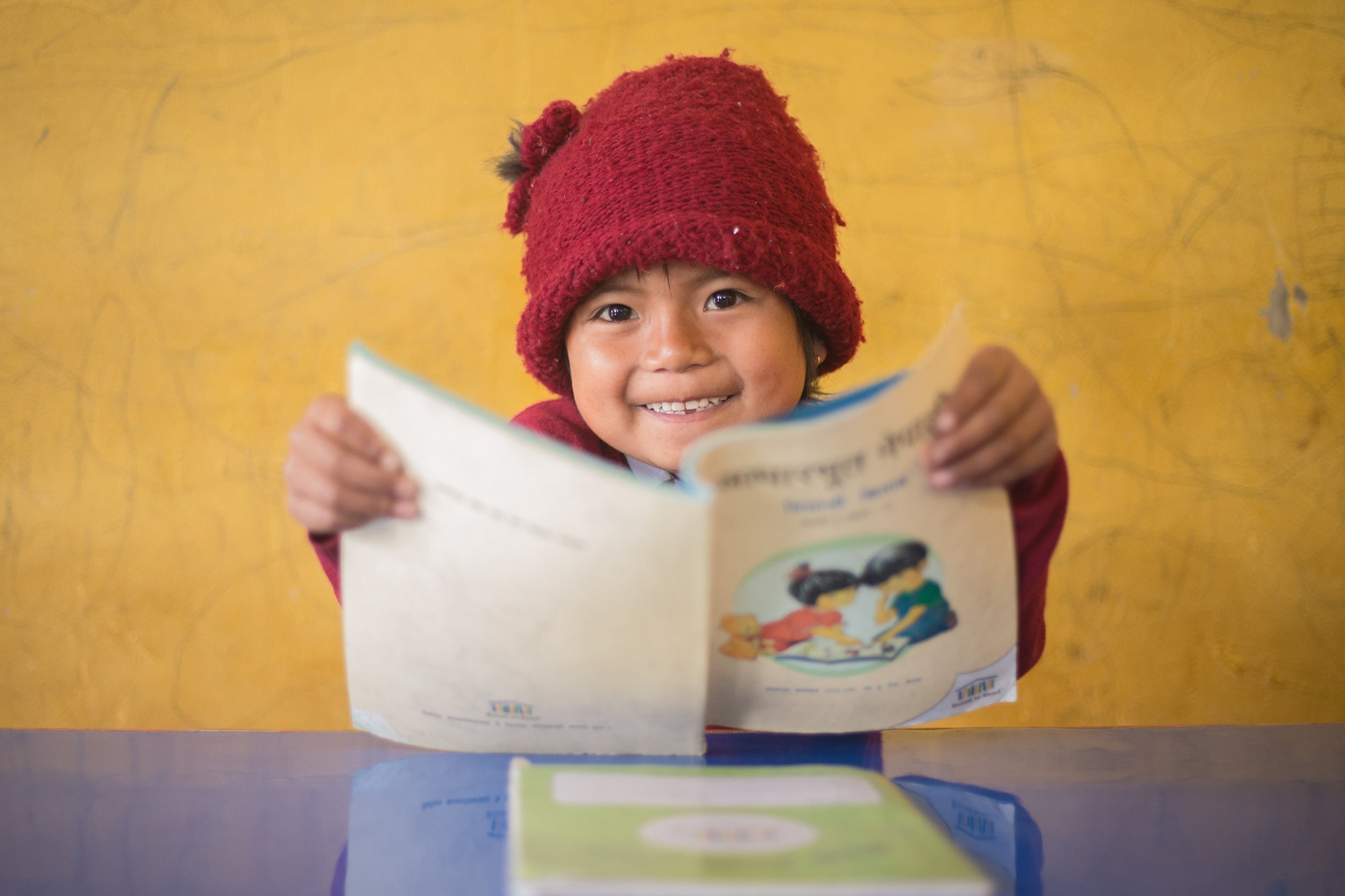 Child in red knitted hat holds open colorful childrens book on World Literacy Day