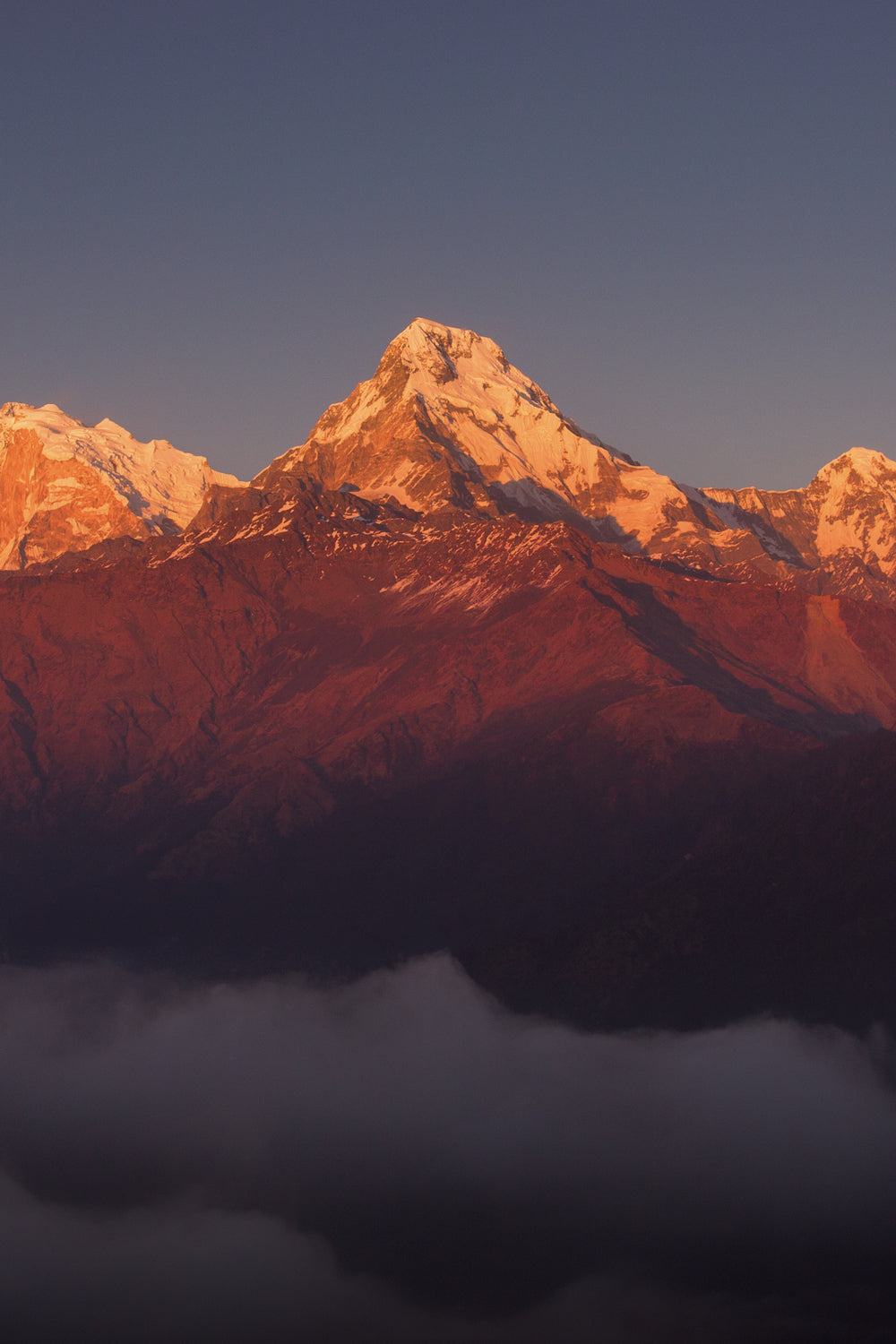 Sunset over a Nepal mountain range with snow-capped peaks. The top of the peaks are golden and low hanging clouds are settling at the base of the mountains.