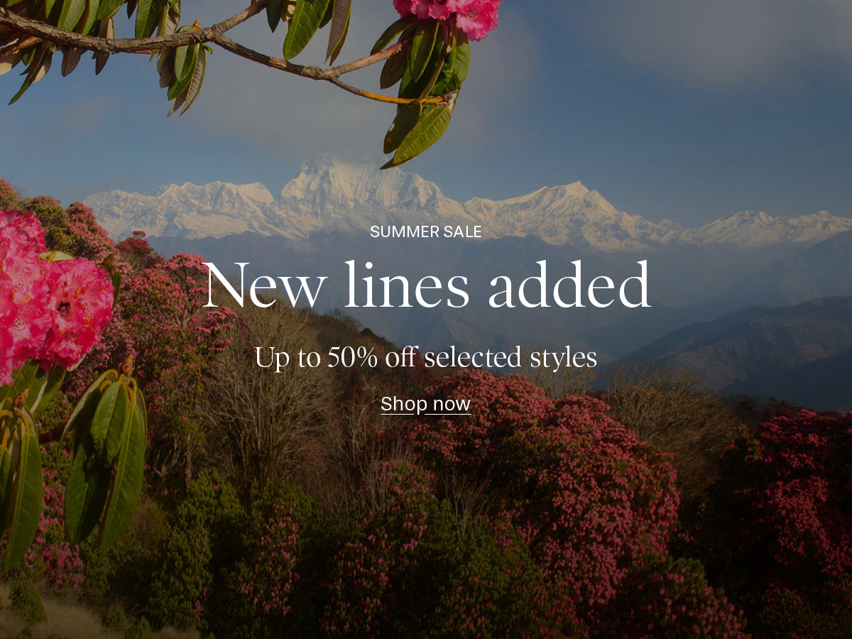 A promotional banner featuring a scenic mountain landscape with snow-capped peaks, pink flowering bushes, and hanging green leaves. White text overlays read 'SUMMER SALE', 'New lines added', 'Up to 50% off selected style', and 'Shop now'.