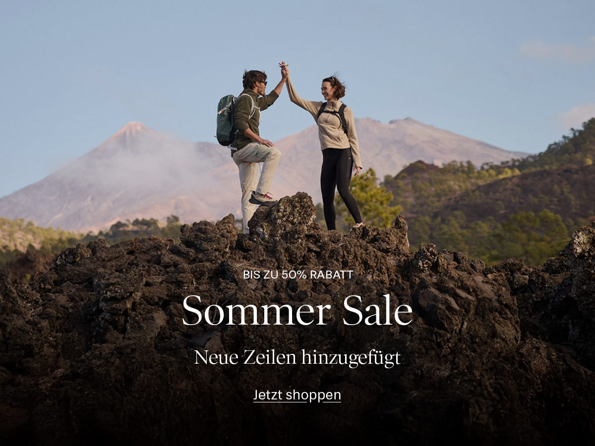 A promotional outdoor scene showing two hikers standing on dark volcanic rock with mountains in the background. Large overlaid text reads 'Sommer Sale' and 'Bis zu 50% Rabatt' with 'Jetzt shoppen' below.