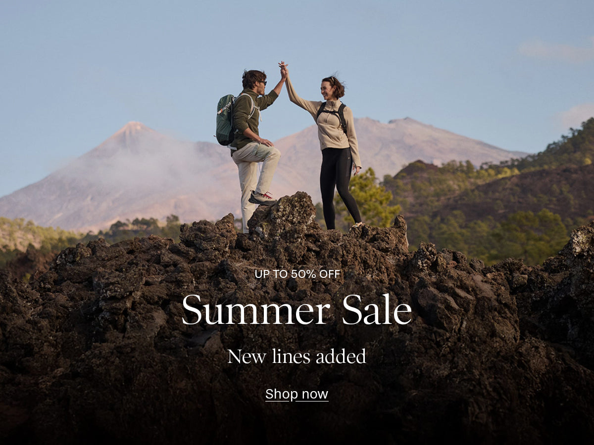 A promotional banner featuring a couple hiking and high-fiving on dark volcanic rocks with mountains in the background. White text overlays read 'UP TO 50% OFF Summer Sale New lines added Shop now'.