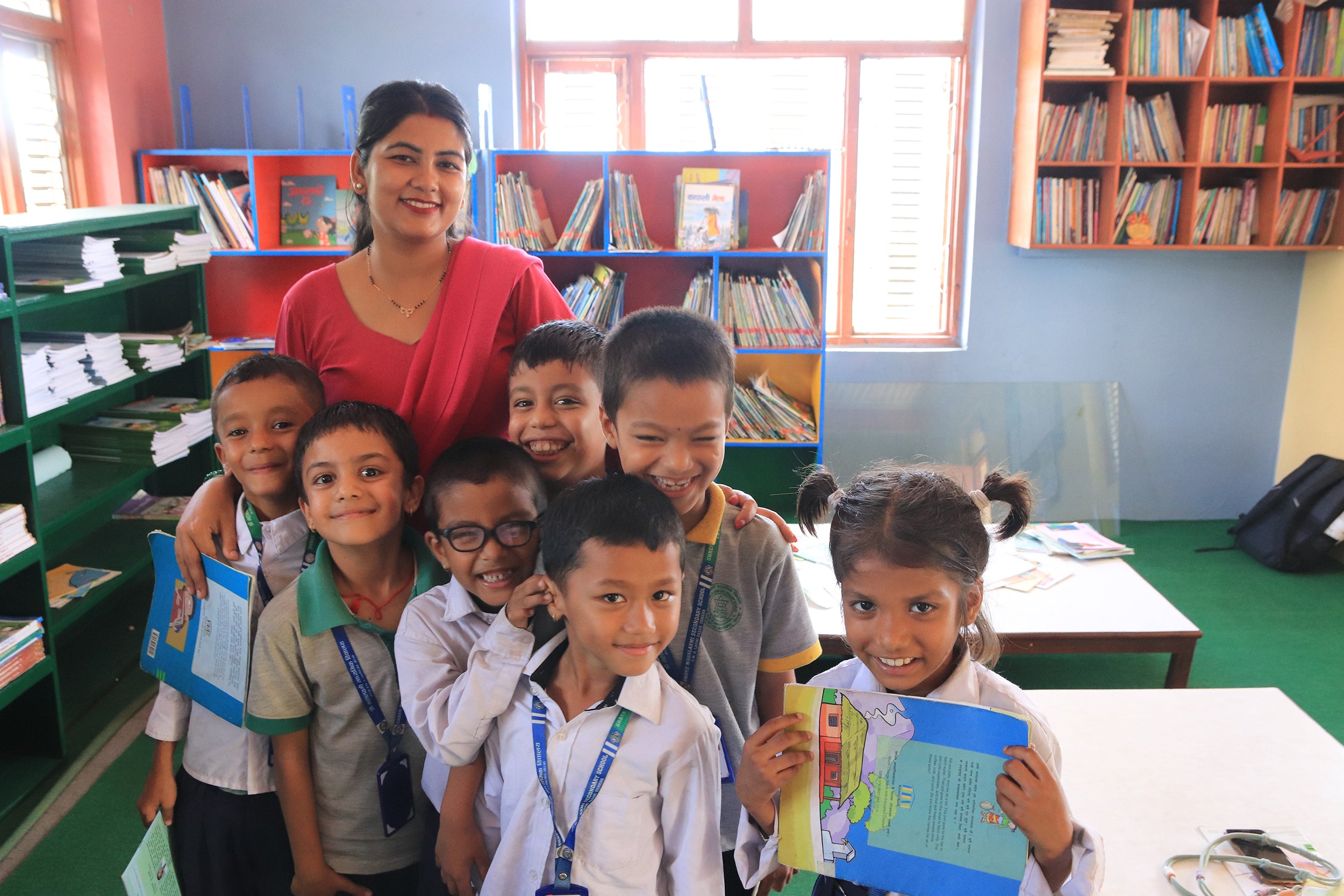 A group of Nepali school children and a teacher in a library setting.
