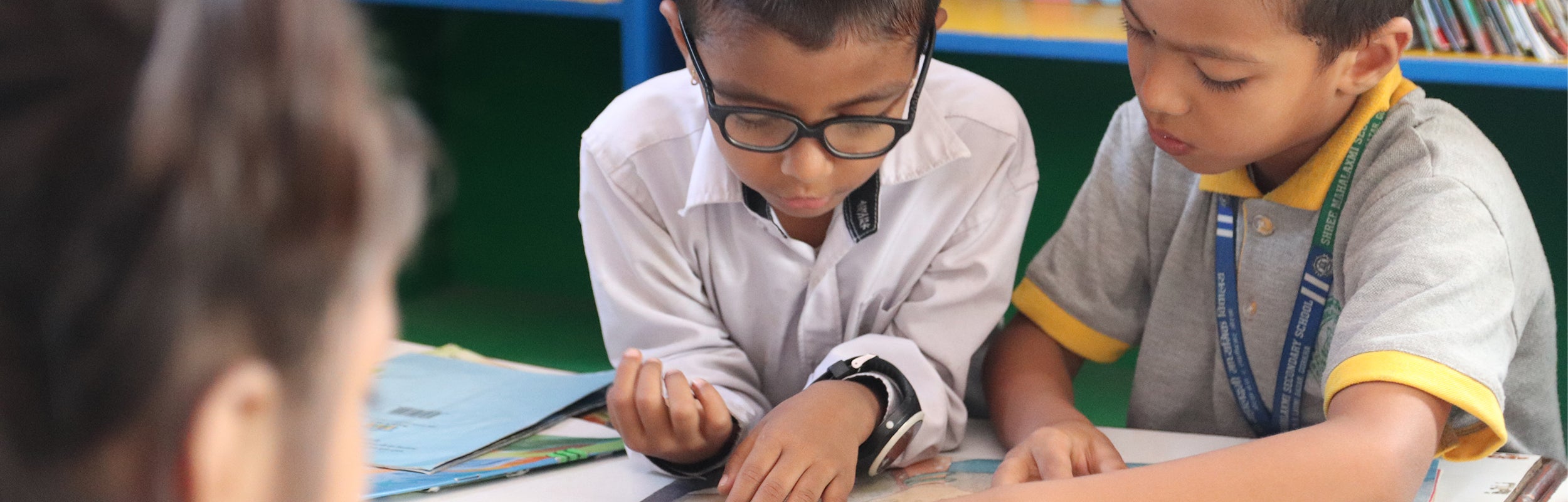 Two Nepali school children sitting at a table with books, engaged in reading or studying.
