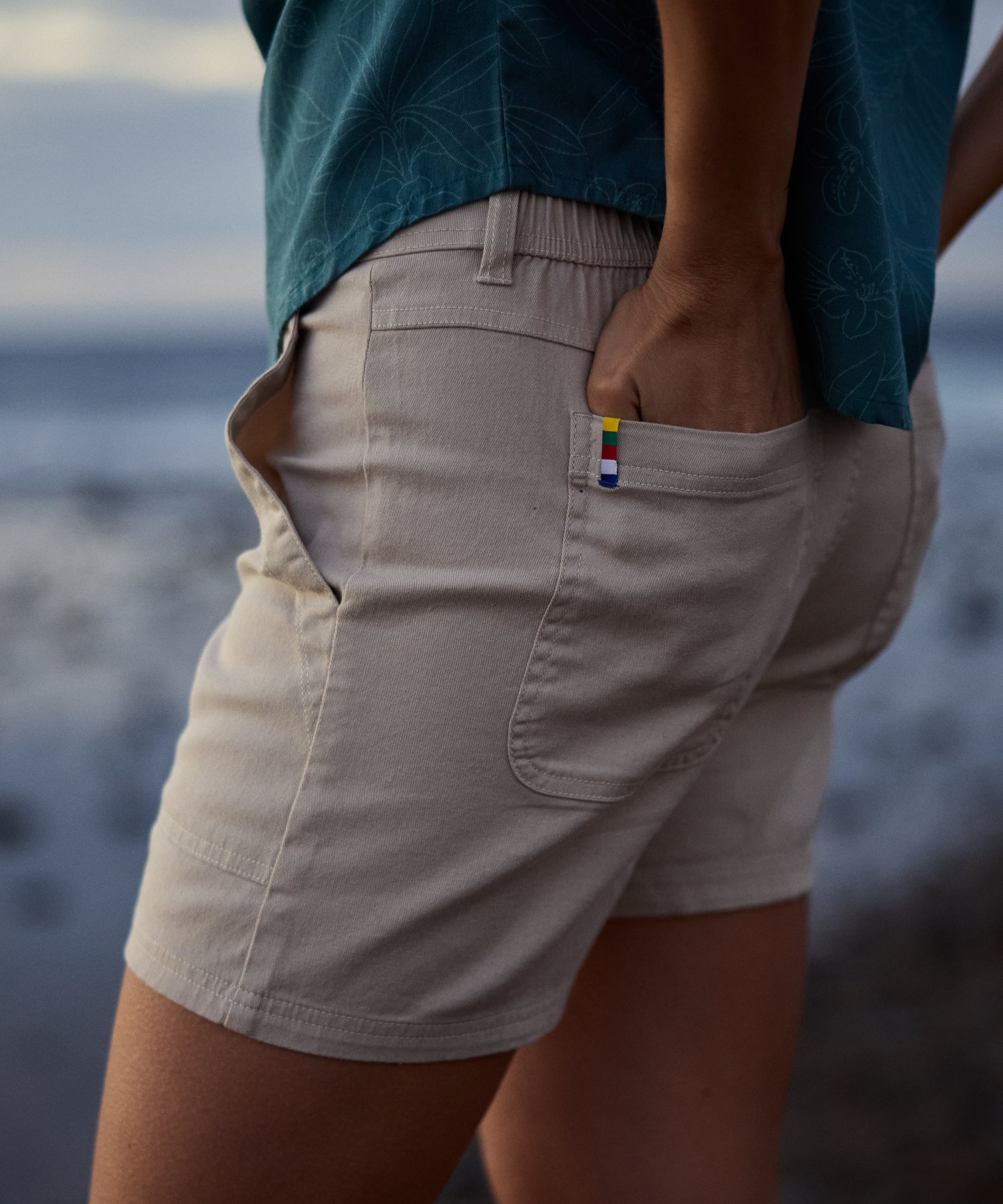 Back view of Dando Shorts - Goa Sand: beige cotton relaxed fit with rainbow flag patch on pocket
